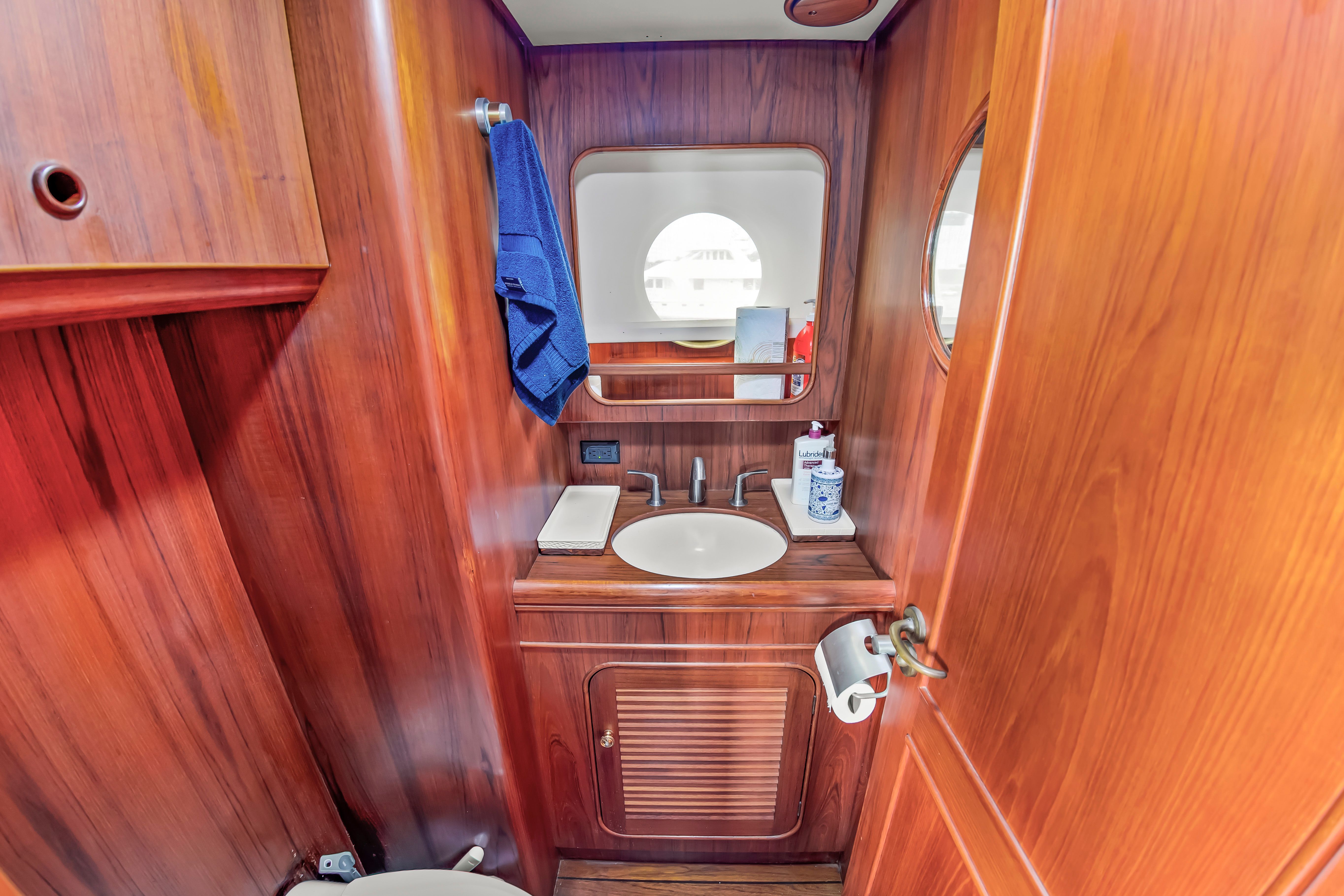 A yacht bathroom with wood paneling, sink, mirror, and porthole, creating an elegant atmosphere.