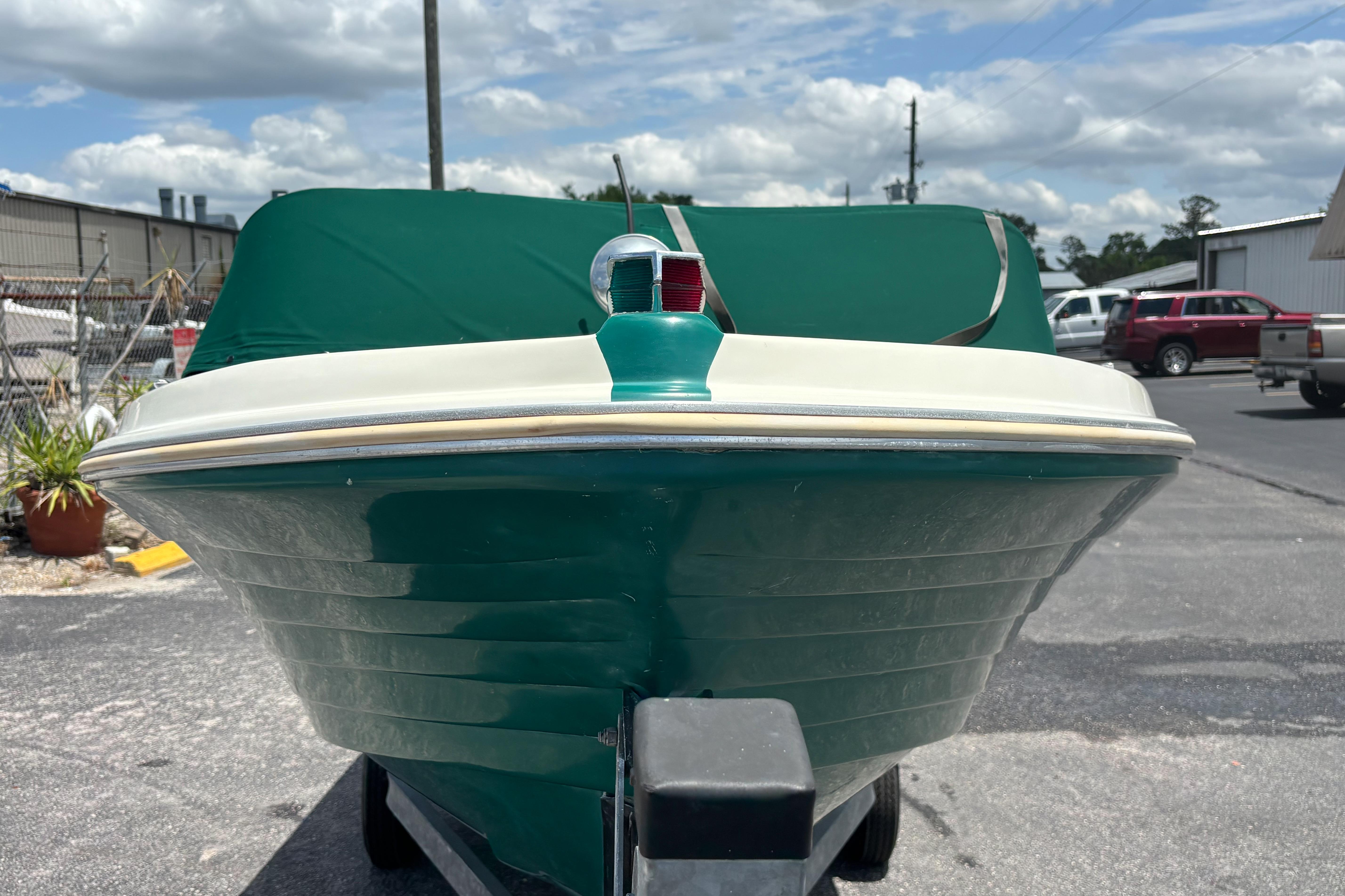1966 Mohawk 15 boat with green cover, parked outdoors under a cloudy sky.