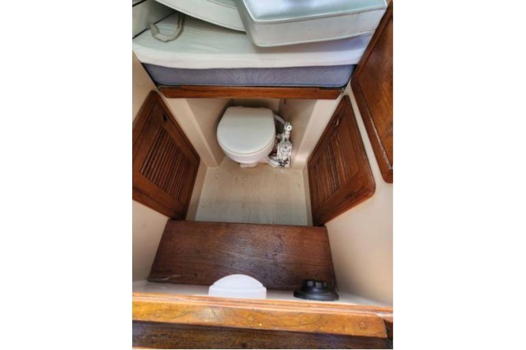 1985 Wasque Down East Cruiser interior with compact marine toilet and wooden cabinetry.