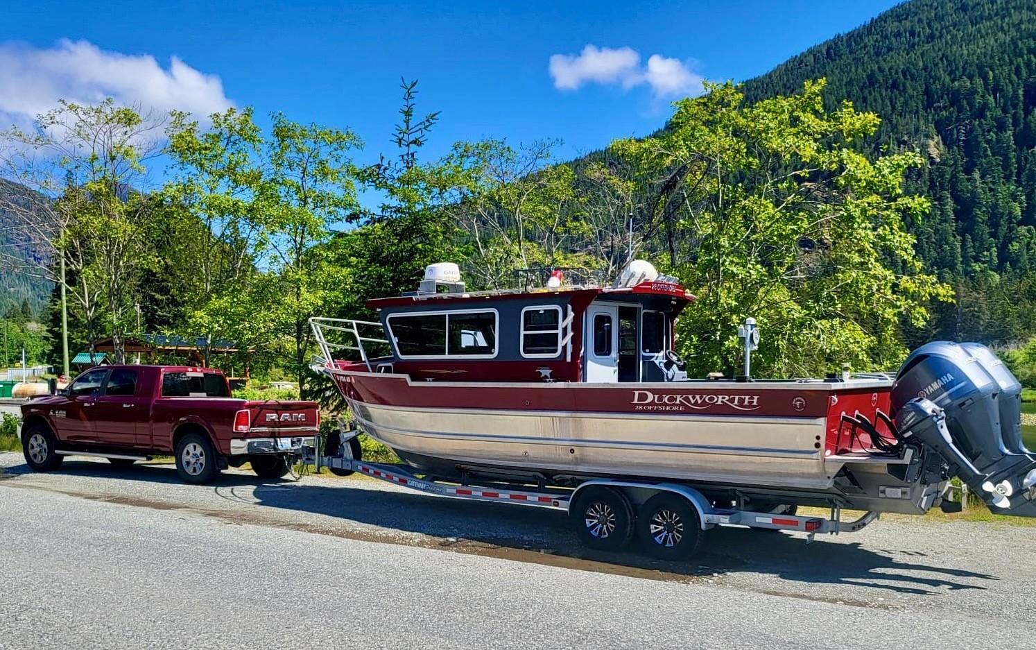 2018 Duckworth 28 Offshore boat on trailer, towed by a red Ram truck, scenic mountain backdrop.