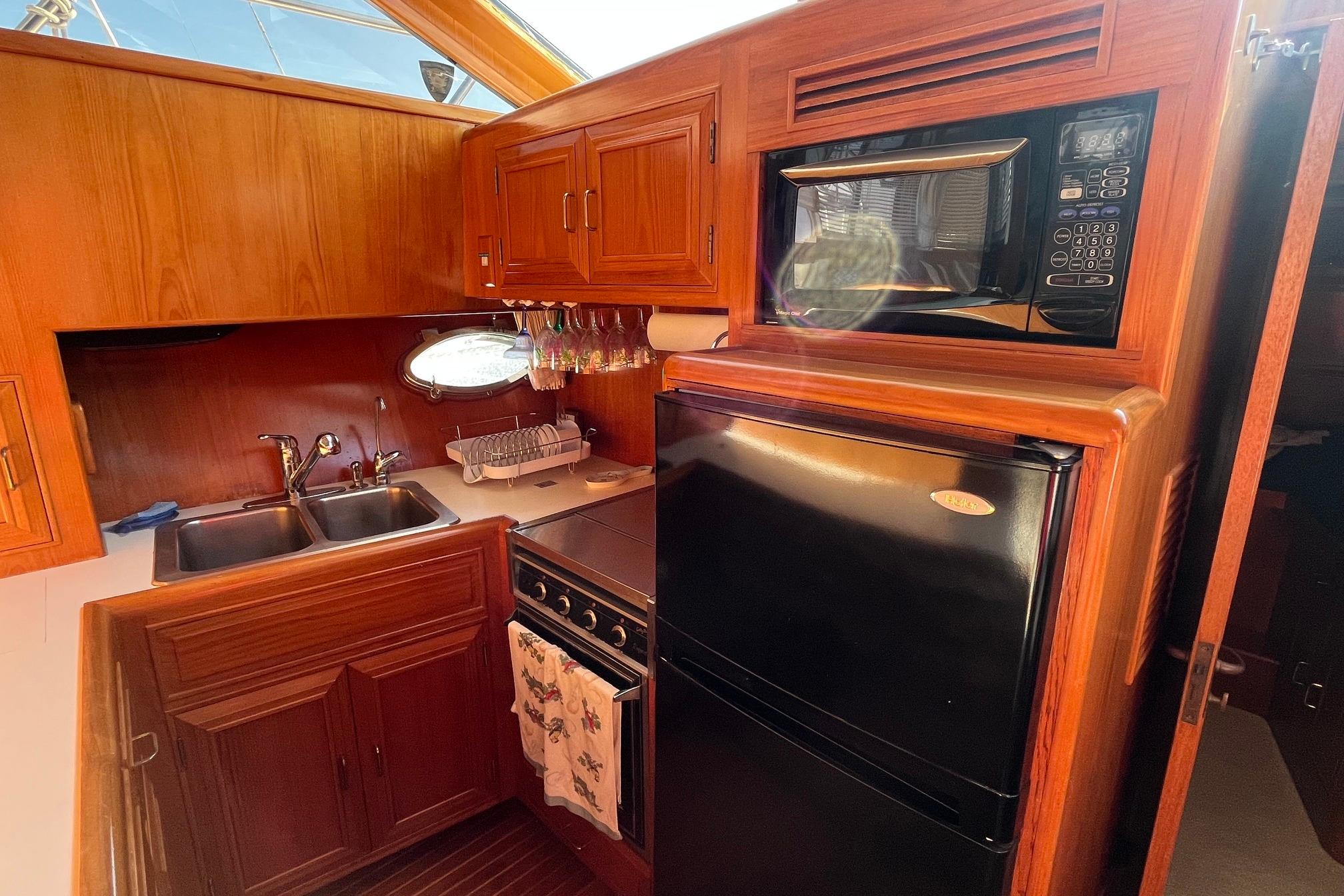 1989 Ocean Alexander 440 Sundeck CPMY galley with wood cabinetry, microwave, and refrigerator.