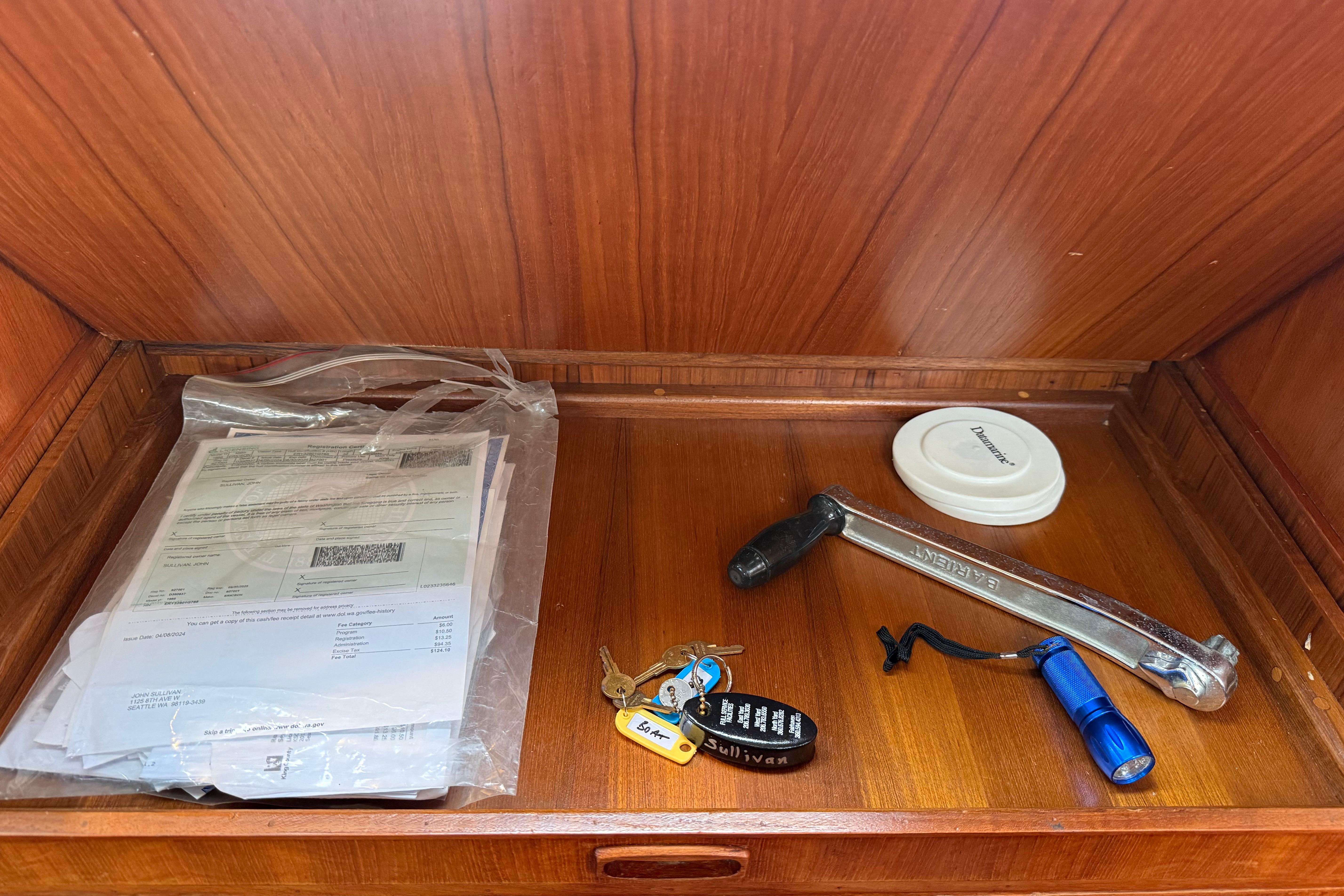 Wooden drawer with documents, keys, wrench, flashlight, and a lid on an Ericson 32-200, 1988.