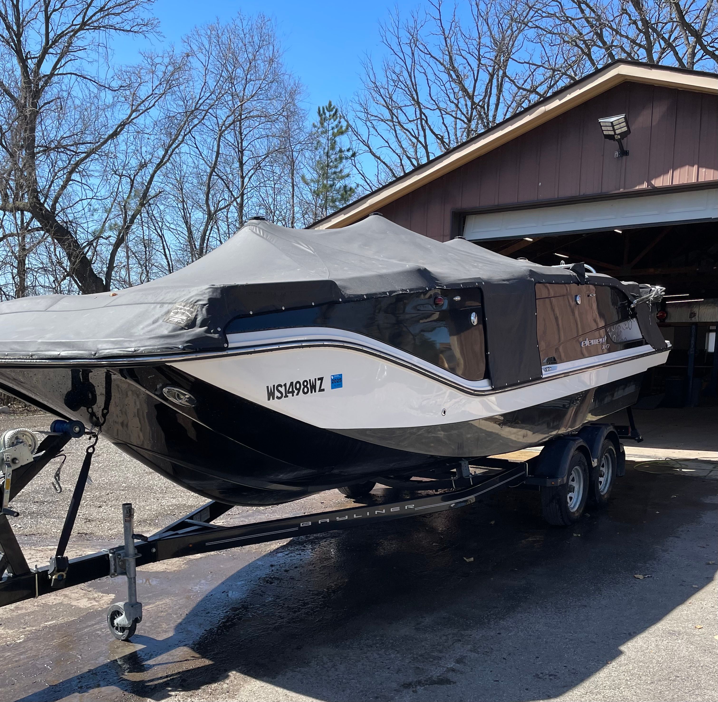 A 2016 Bayliner Element XR7 on a trailer in front of a garage.