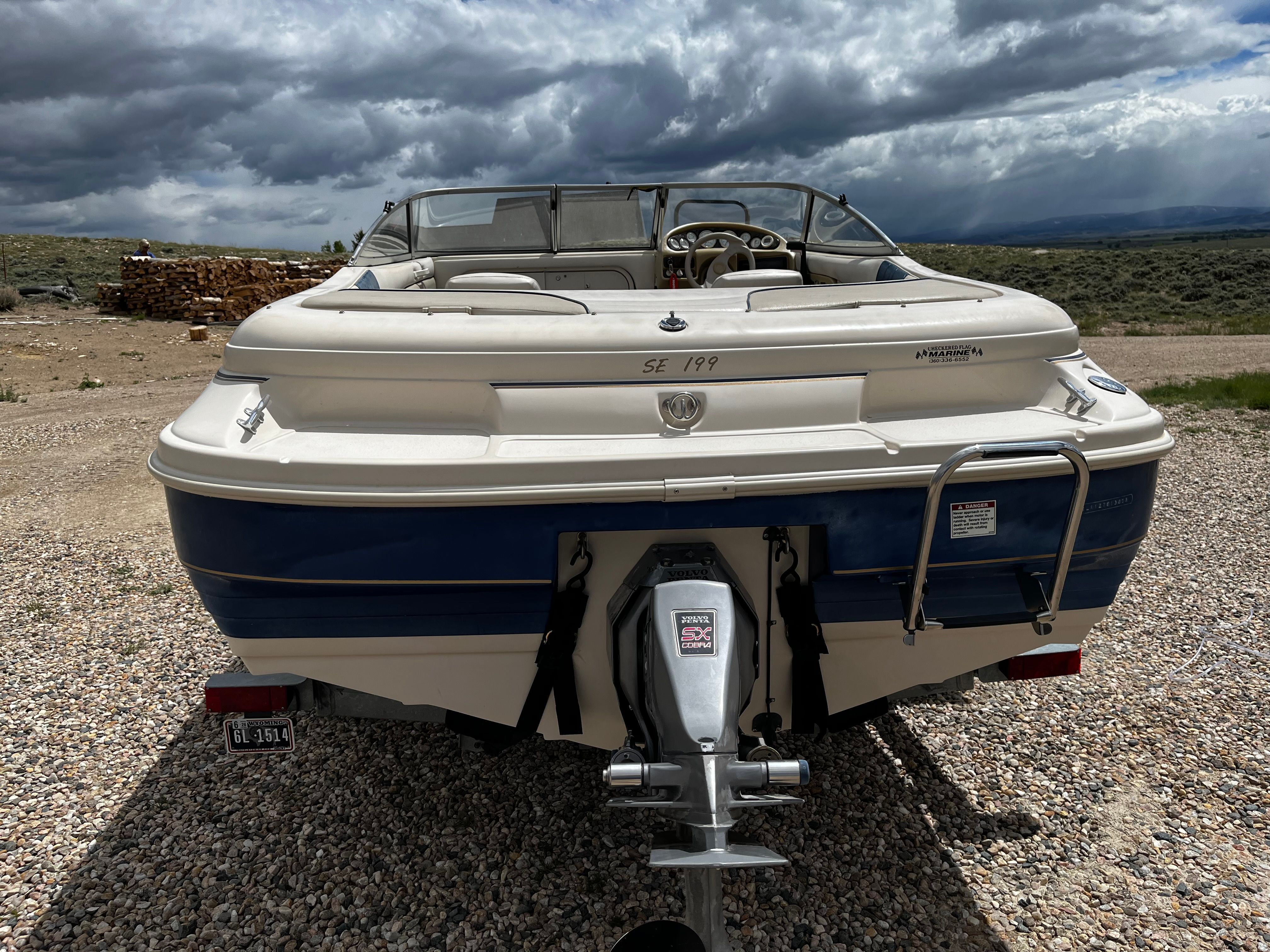 A 1998 Glastron SE199 boat on a trailer in a gravel lot under a cloudy sky.