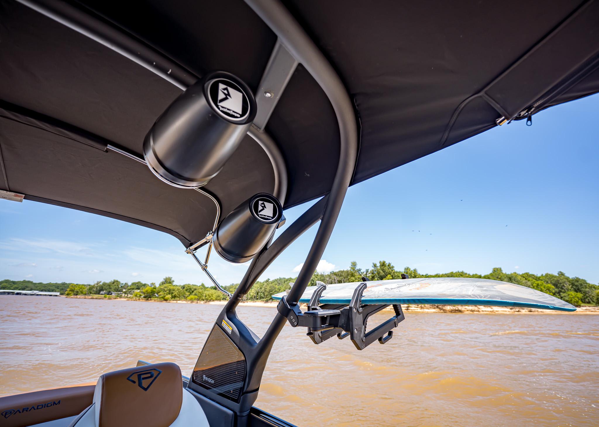 2025 Paradigm 236 boat with speakers and surfboard rack on a sunny day.