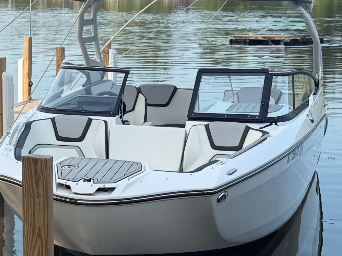 A sleek, modern boat with an open deck and glass windshield, docked at a calm pier.