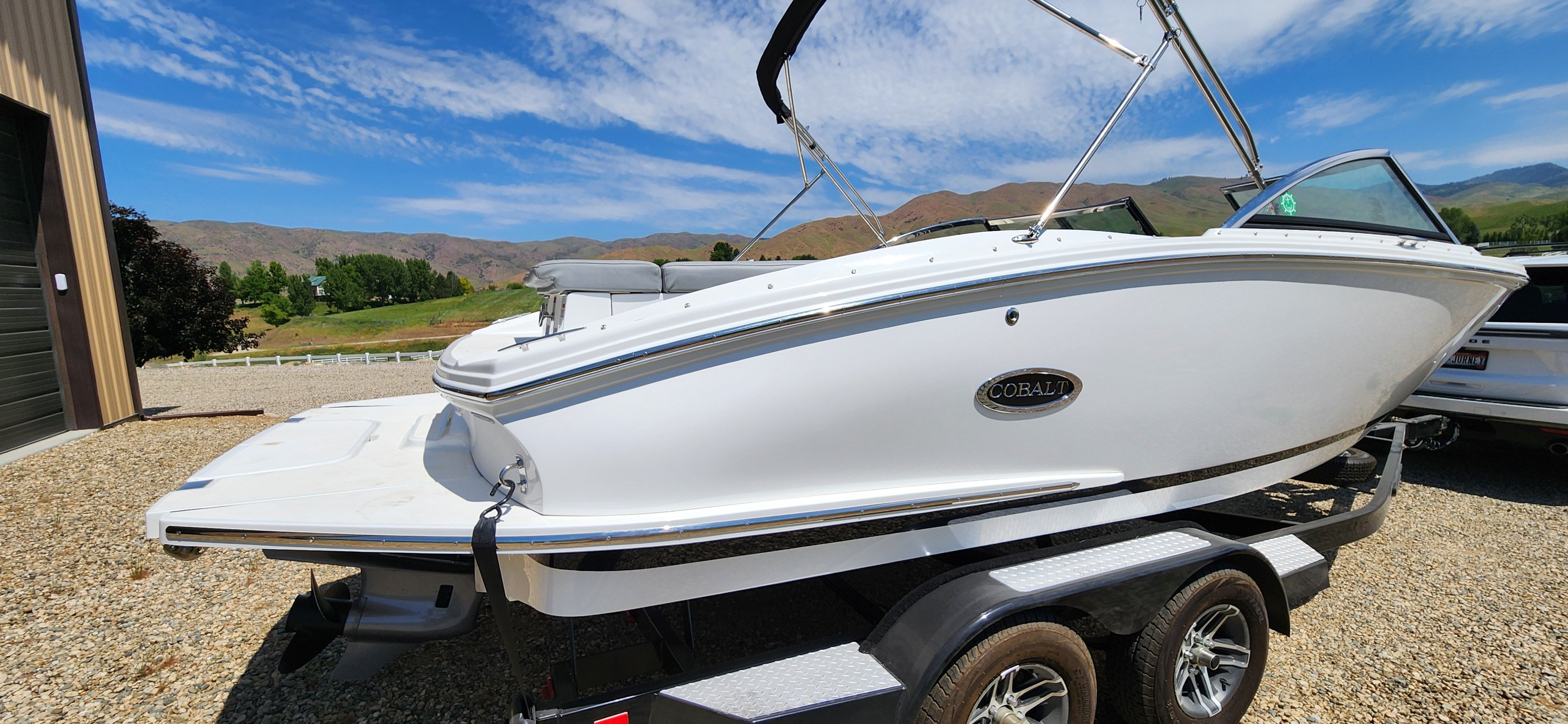 A white Cobalt CS22 boat is on a trailer in front of a scenic landscape.