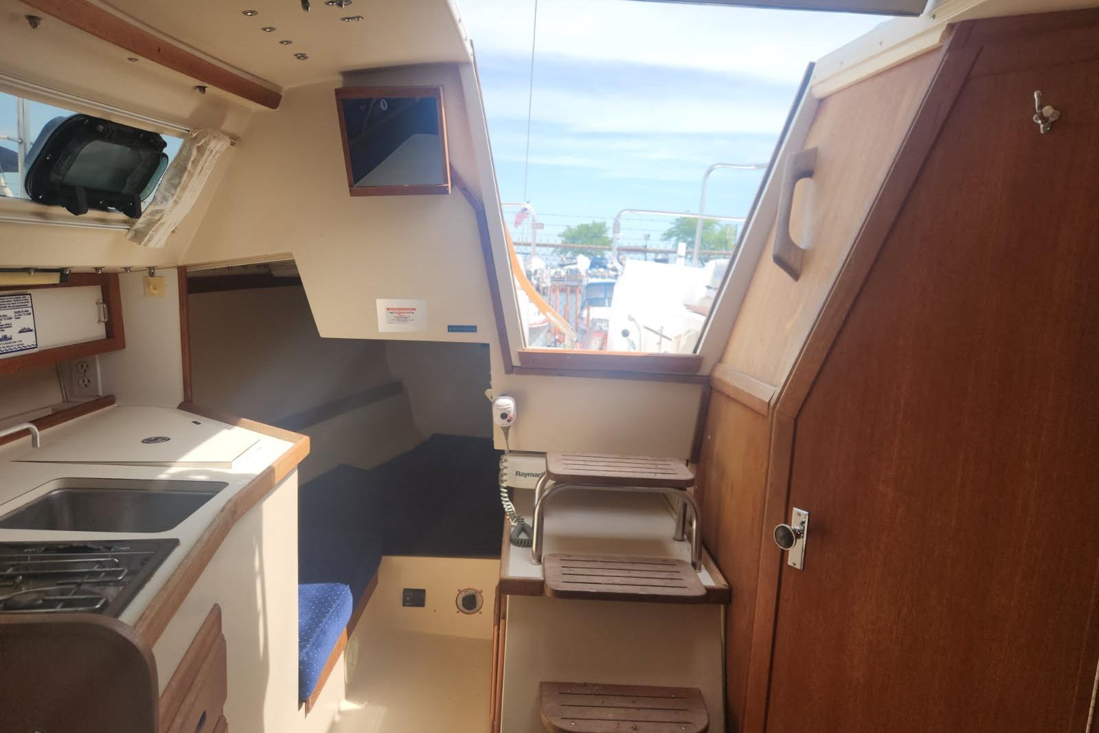 Interior of a 1990 Catalina Capri sailboat featuring a compact kitchen and wooden steps.