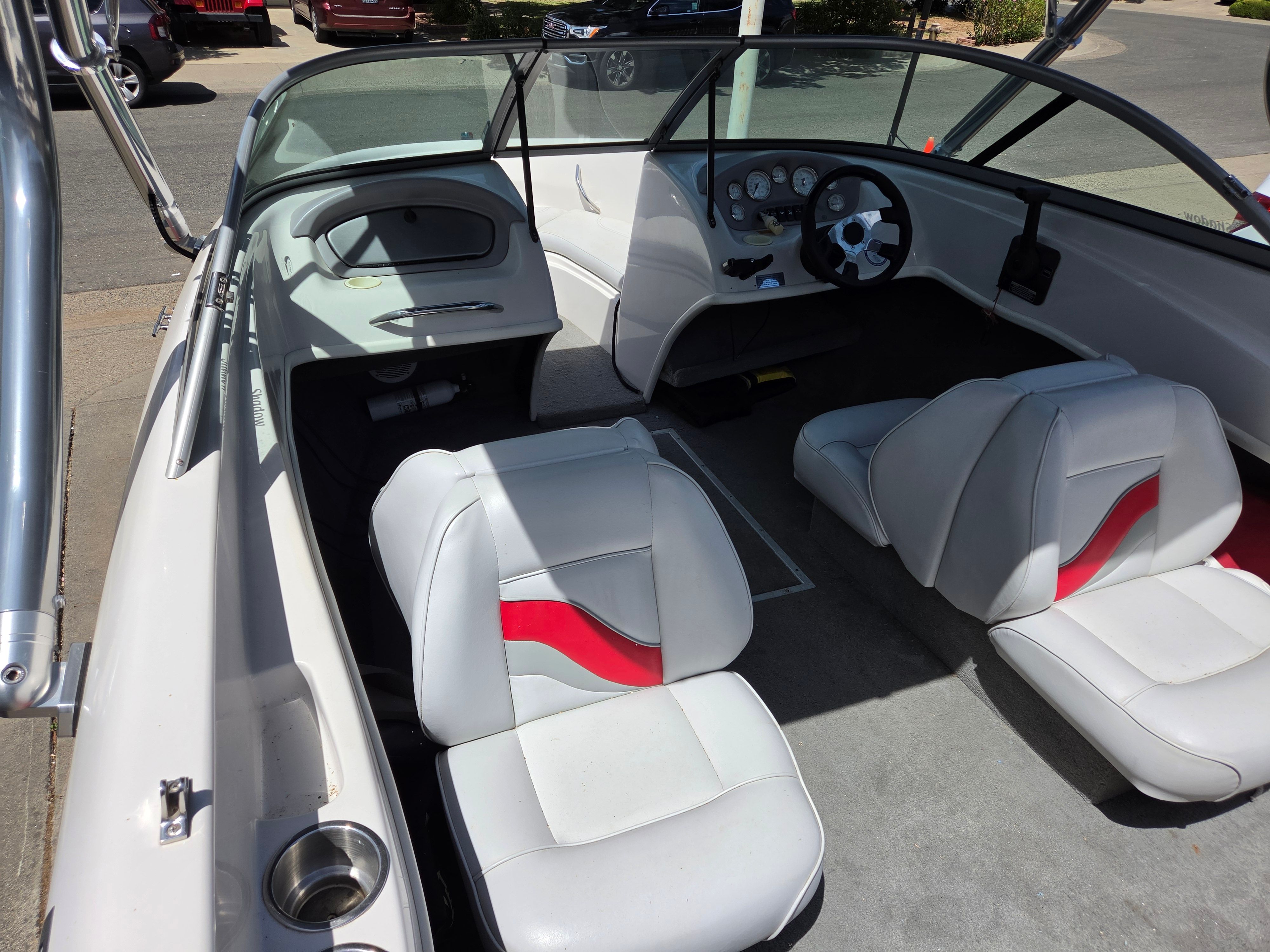 Interior view of a boat with white seats and red accent, steering wheel, and dashboard.