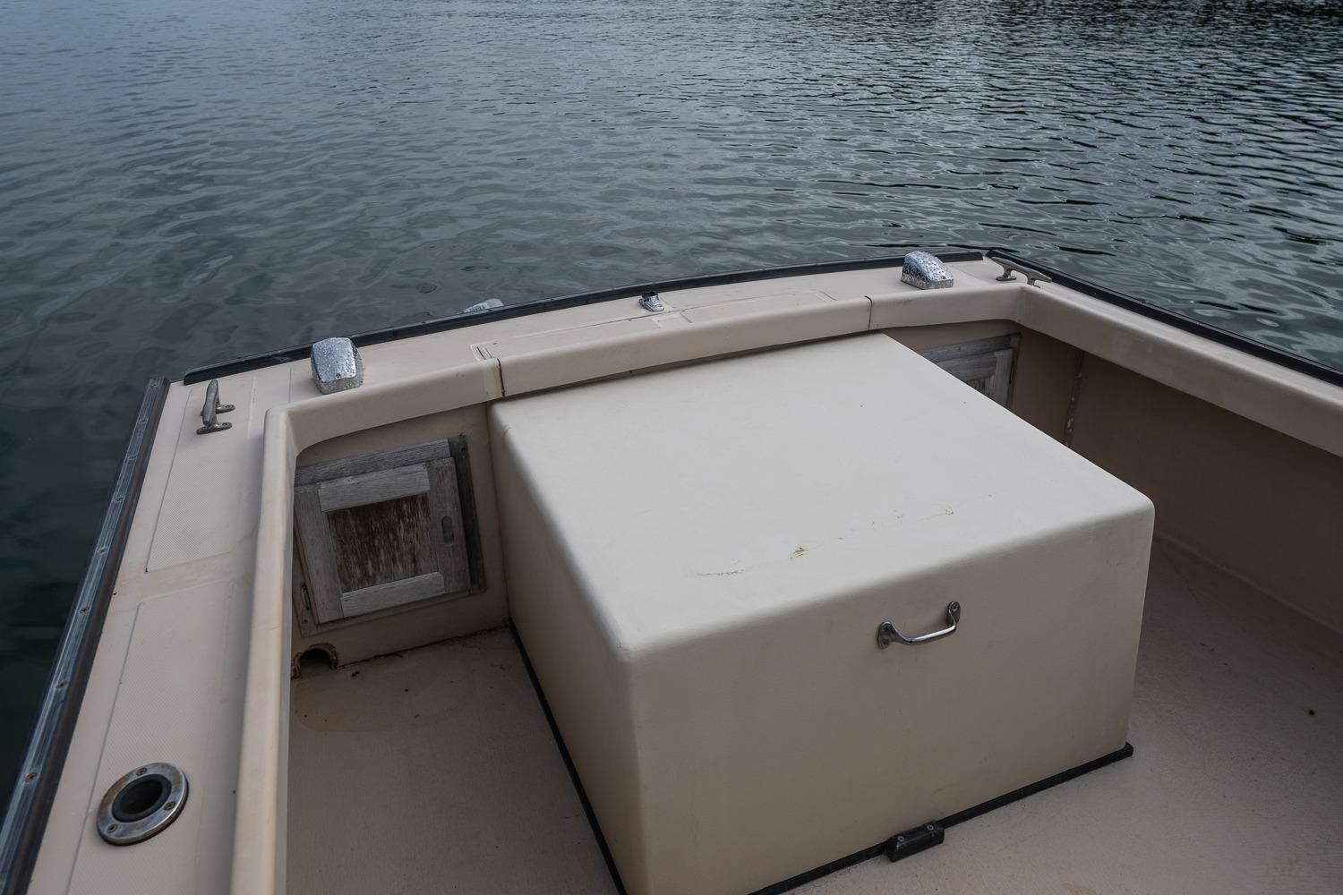 1989 Ellis 24 Open boat interior with storage compartment on calm water.