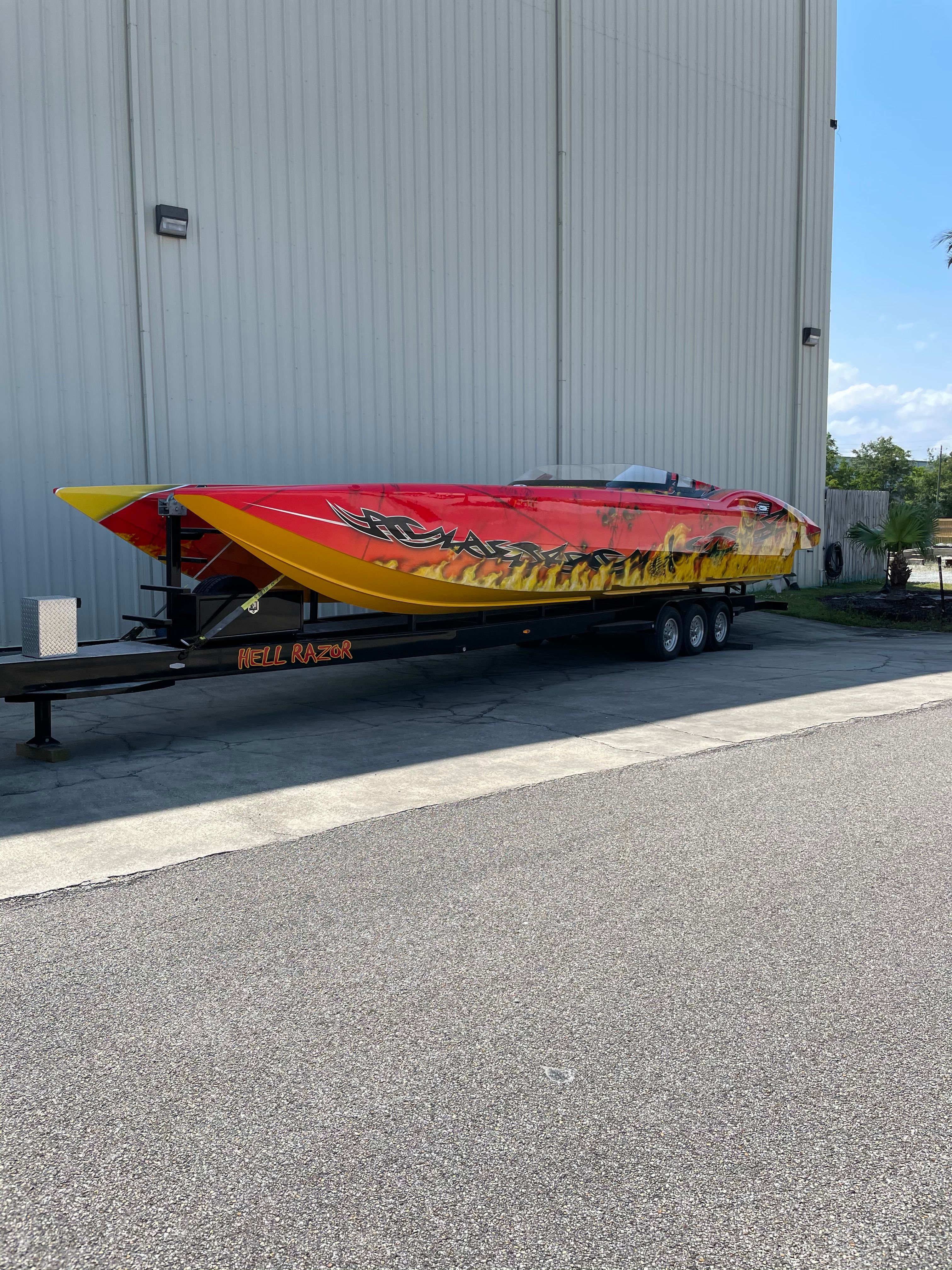 A bright yellow and red high-speed boat on a trailer in front of a large building.