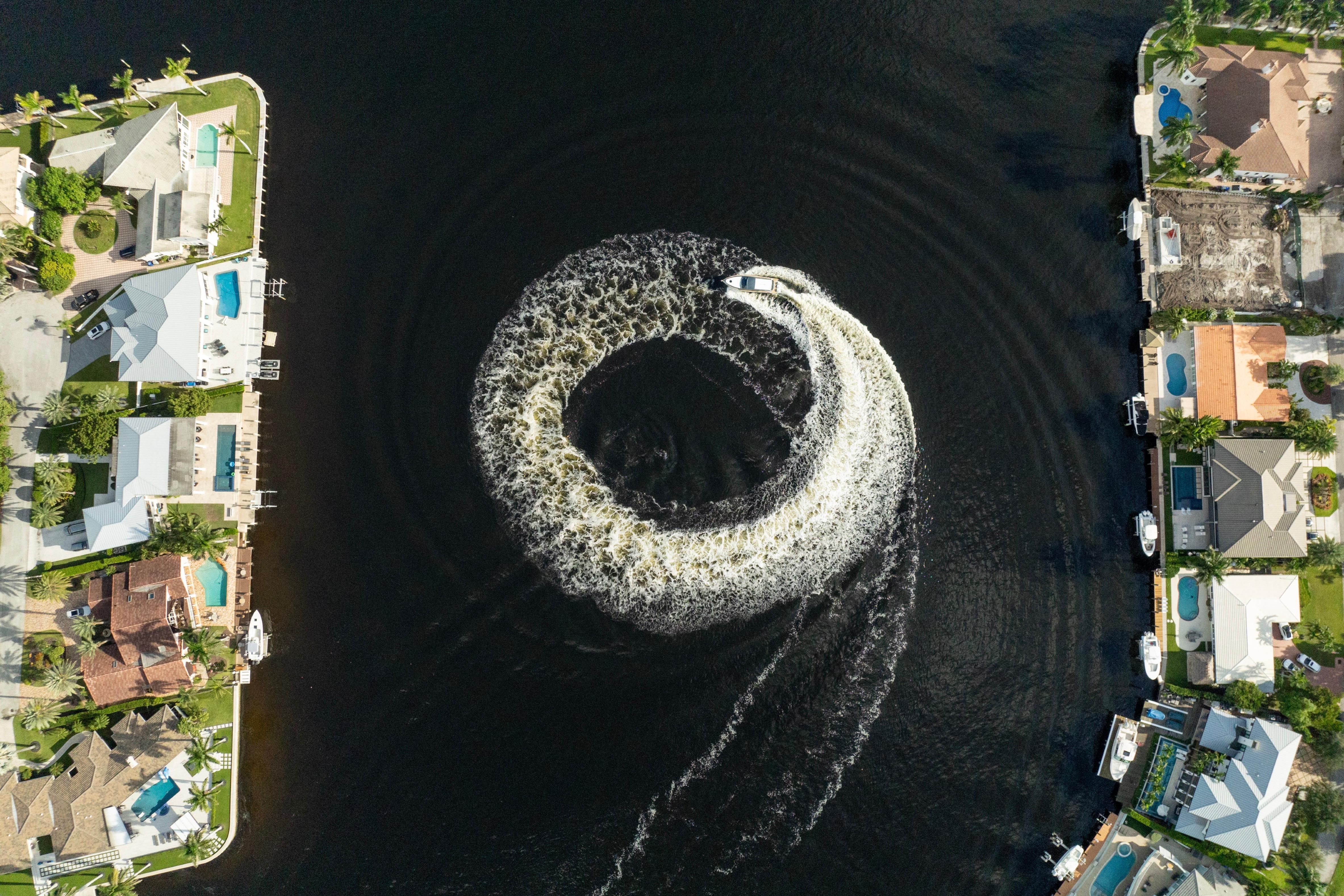Aerial view of Valiatt 410HT boat creating circular wake in canal, surrounded by waterfront homes.