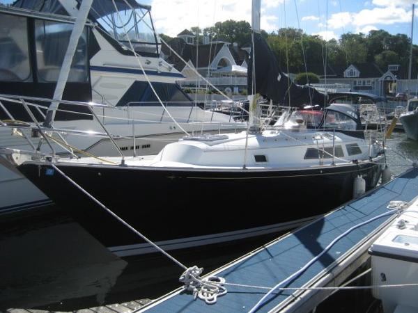 A black sailboat is docked in a marina, surrounded by other boats and buildings.