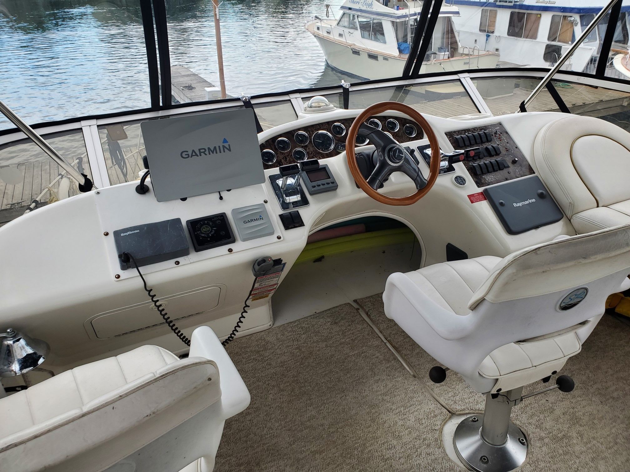 The cockpit of a 1999 Sea Ray 370 Aft Cabin with two white seats and a wooden steering wheel.