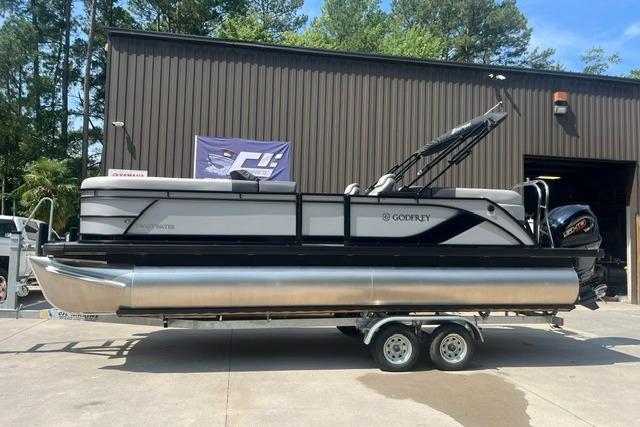 2026 Godfrey Sweetwater 2286 SBC pontoon boat on trailer, parked outside a warehouse.