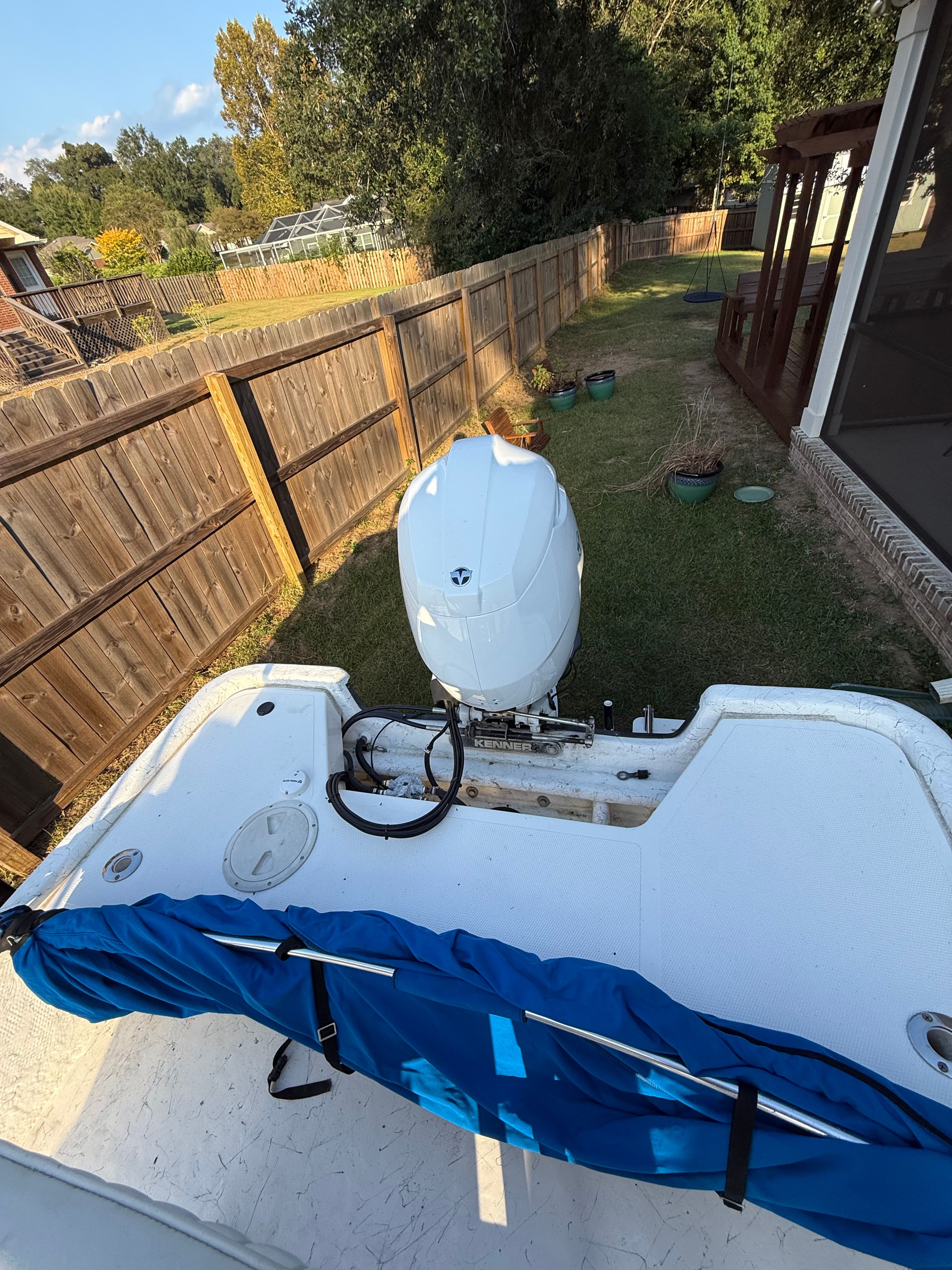 A boat with an outboard motor is on a lawn next to a wooden fence.