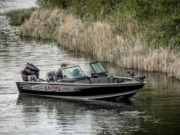 2026 Lund 2075 IMPACT XS boat cruising on a calm river surrounded by reeds.
