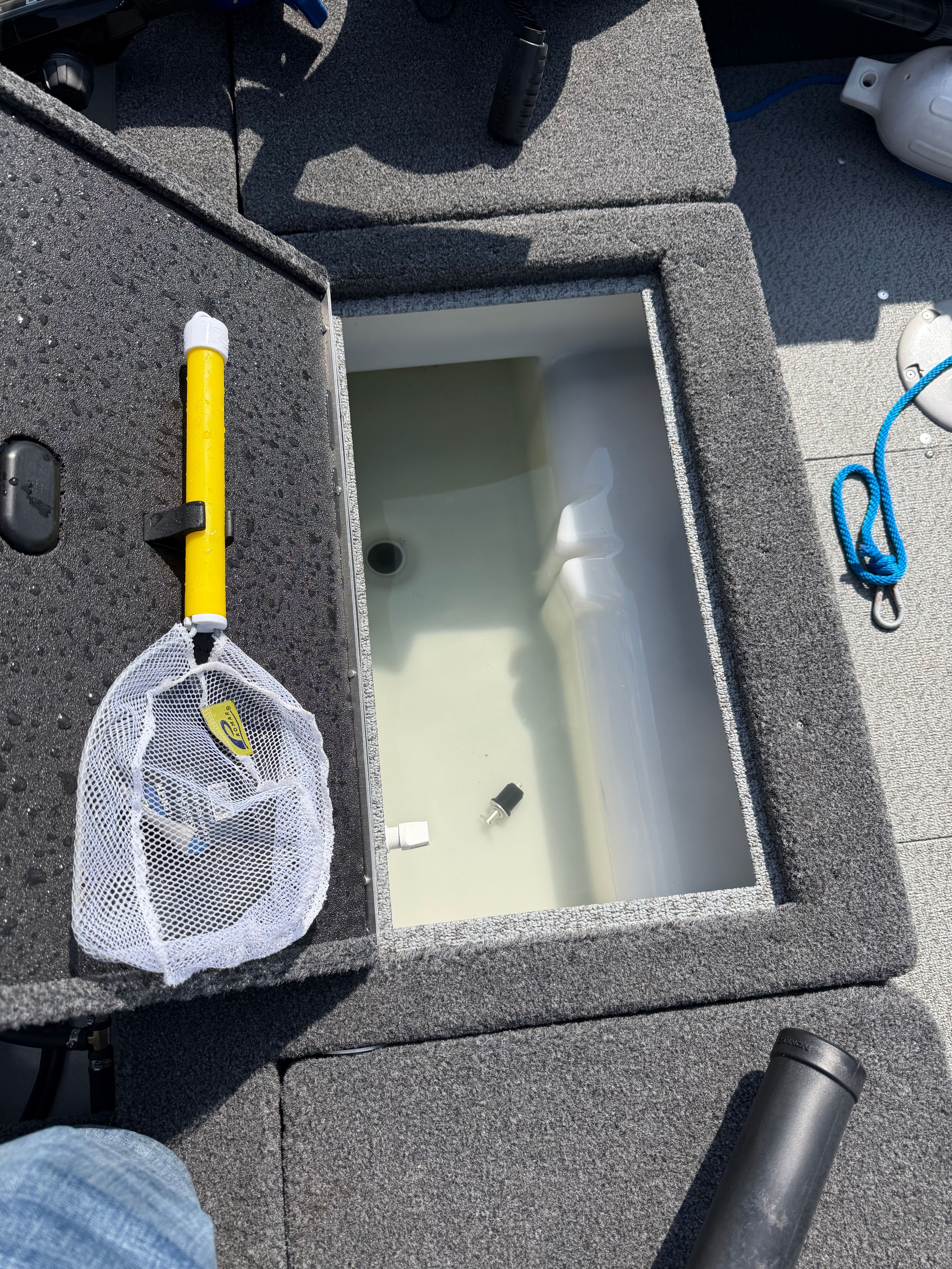 An open storage compartment on a boat with a fishing net beside it.