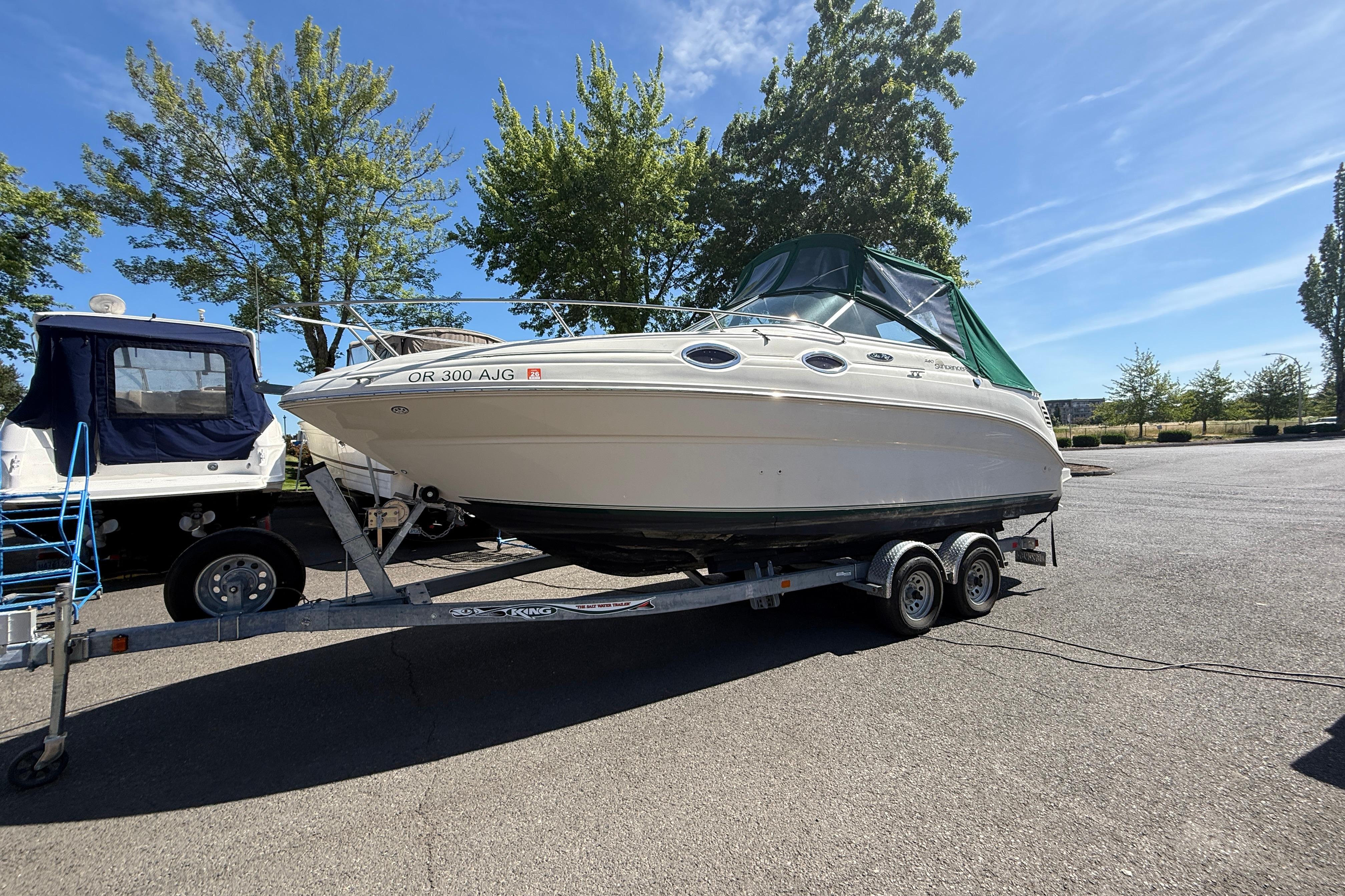 2004 Sea Ray 240 Sundancer boat on trailer, parked outdoors under clear sky.