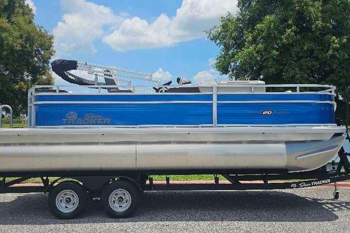 2026 Sun Tracker Fishin' Barge 20 DLX pontoon boat on trailer, blue exterior, sunny day.