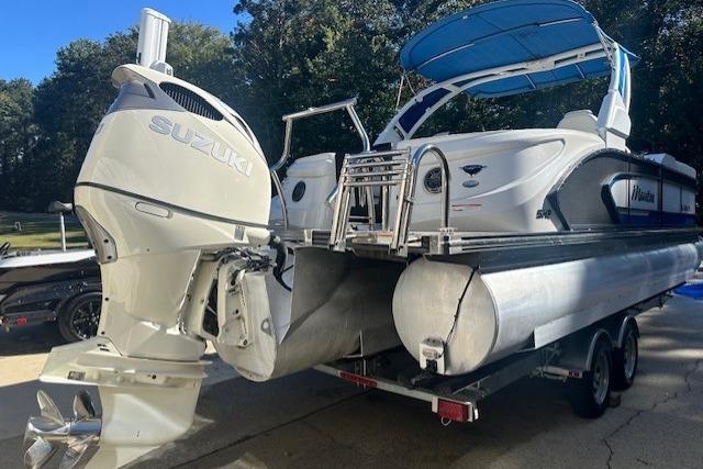 2020 Manitou 25 X-Plode RFW pontoon boat with Suzuki outboard motor, parked on trailer.