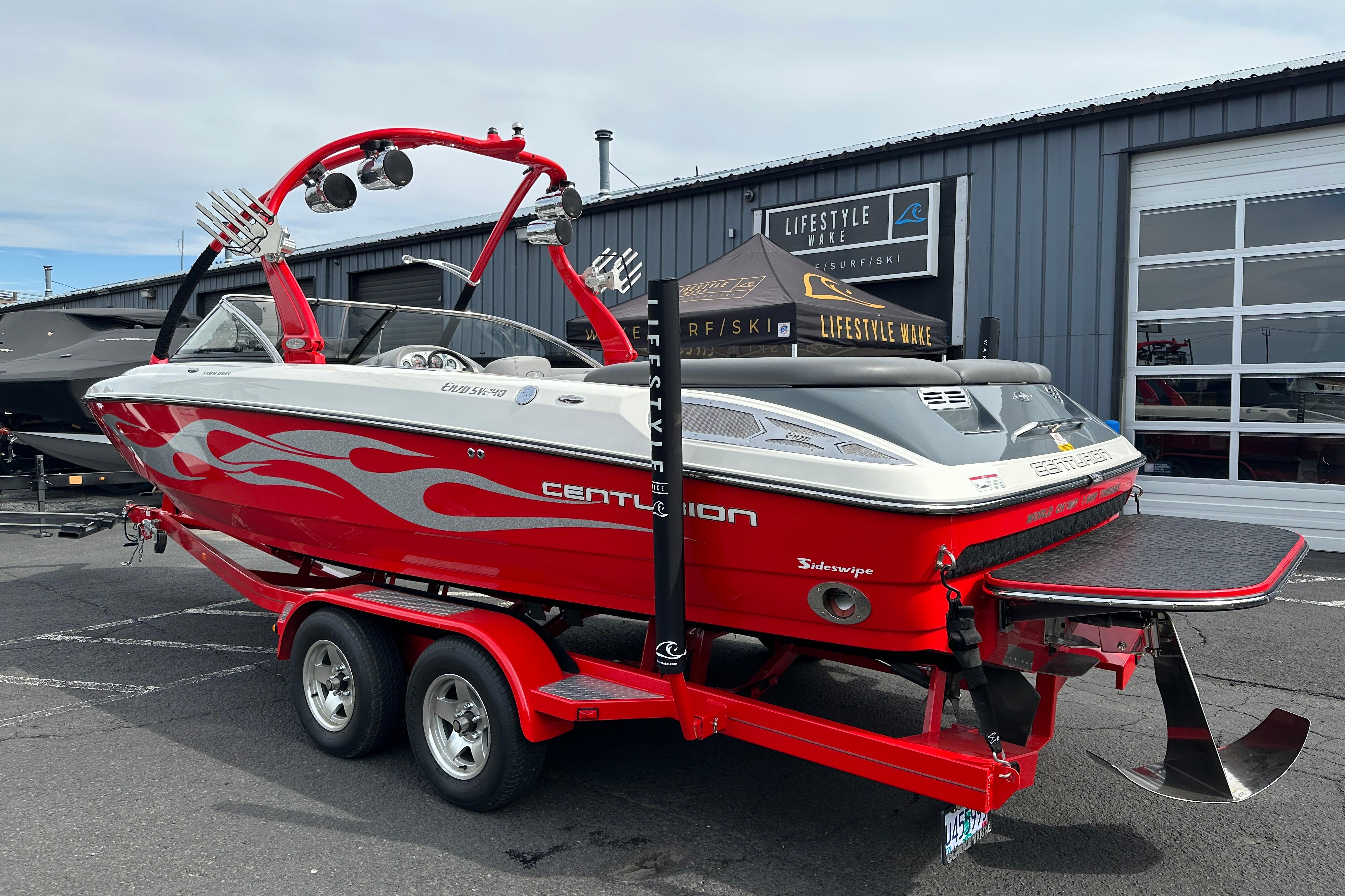 2008 Centurion Enzo SV240 boat with red flame design on trailer, parked outside a building.