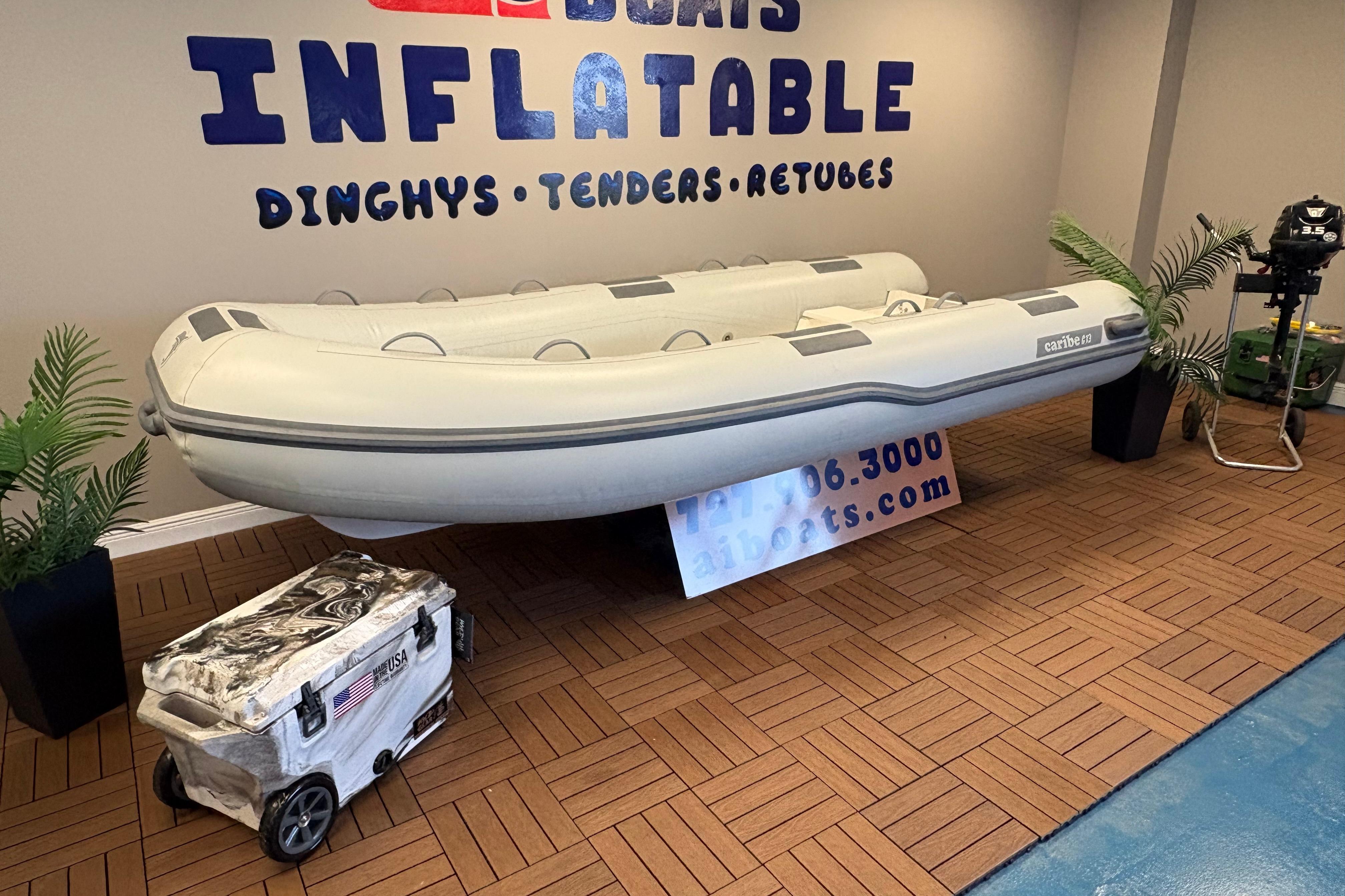 Inflatable Caribe C-13 boat displayed indoors, surrounded by plants and equipment, 2026 model.