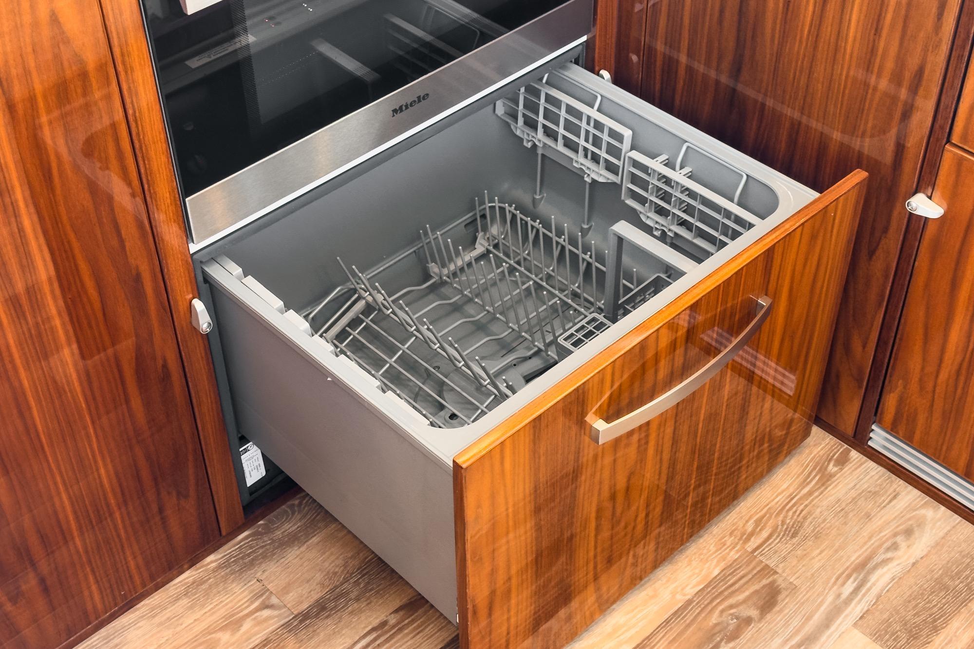 Open dishwasher drawer in 2024 Riviera 5400 Sport Yacht kitchen, featuring wood cabinetry.