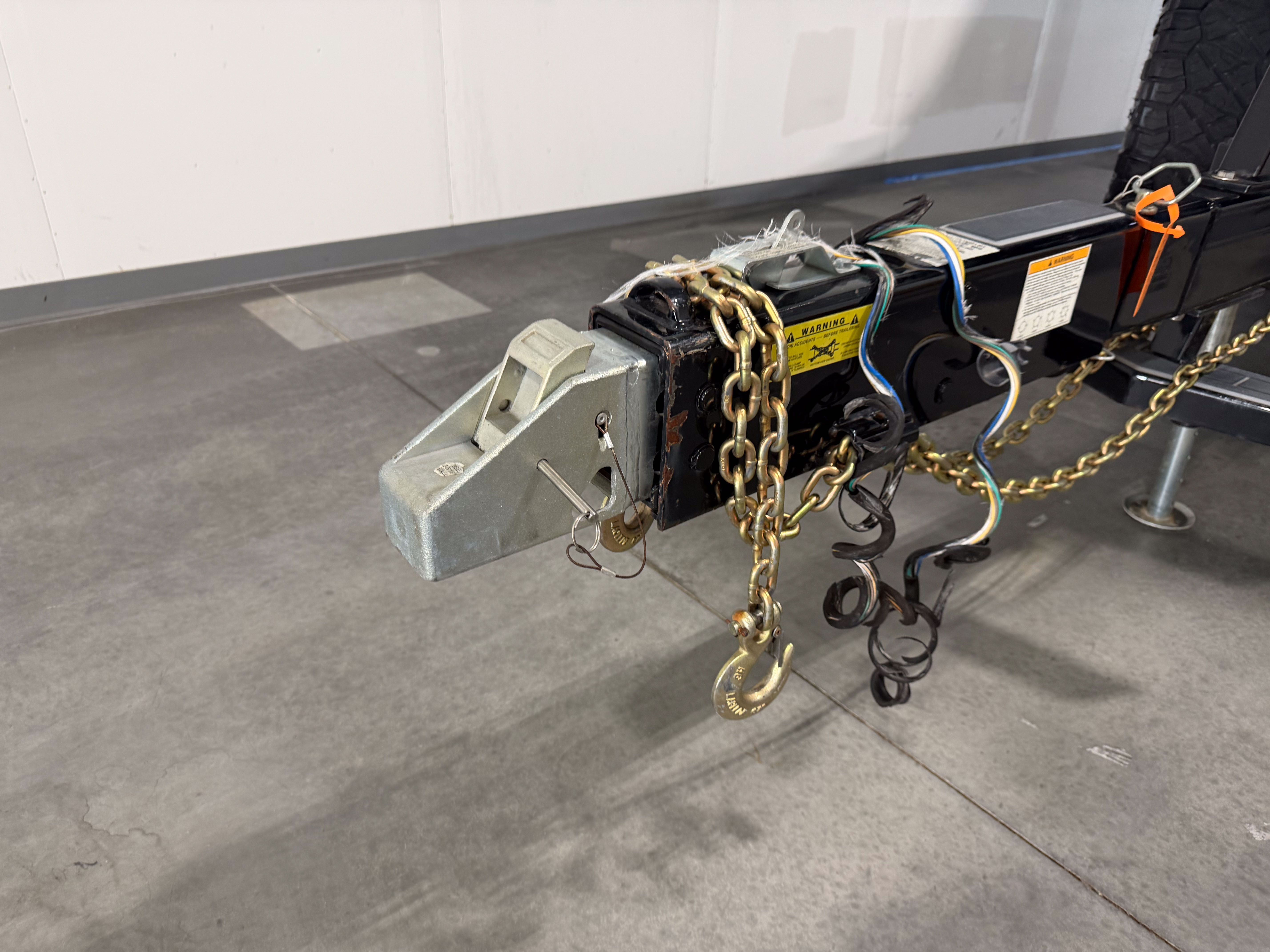 Close-up of a trailer hitch with chains and cables on a concrete floor.