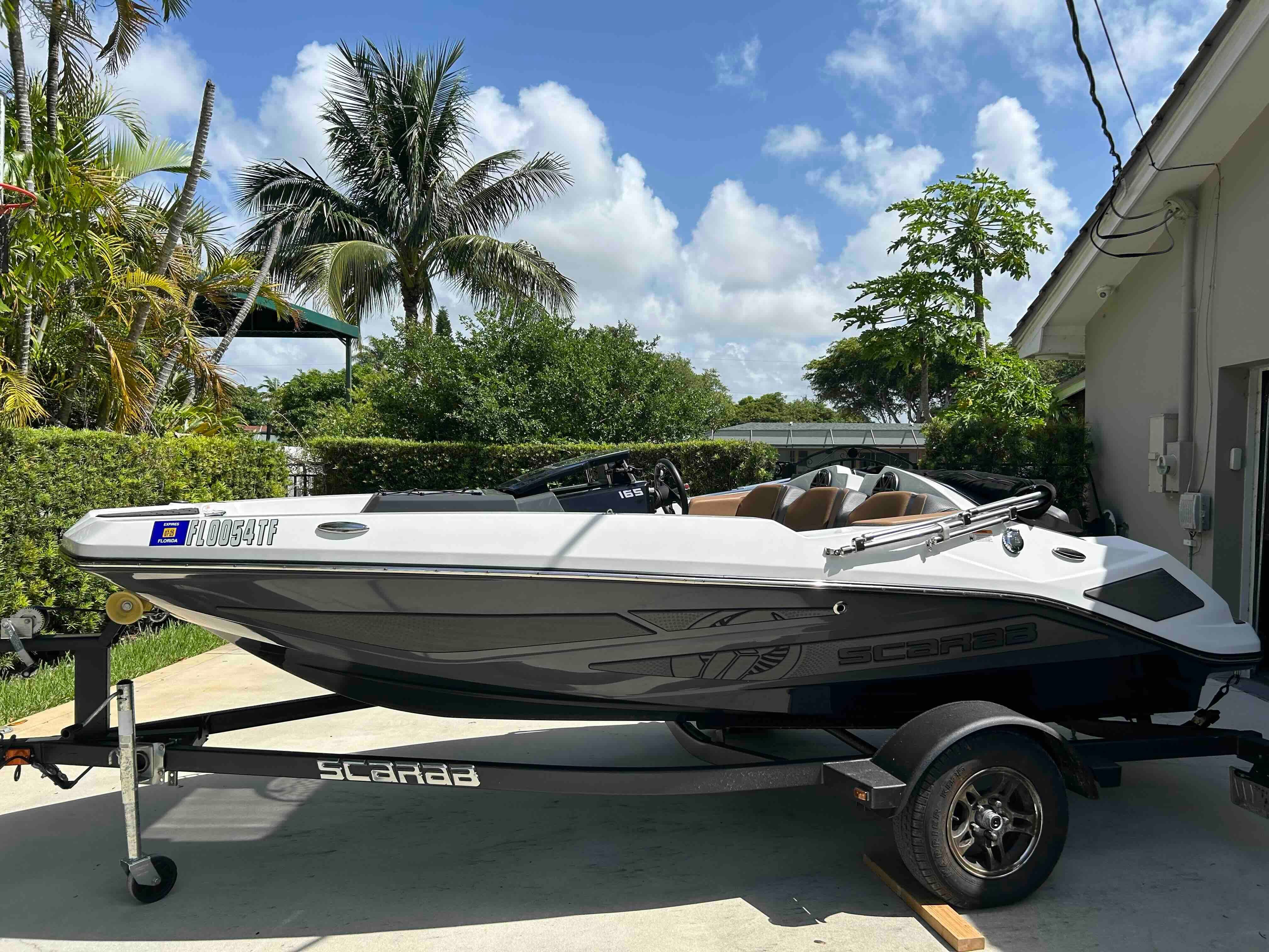 A 2022 Scarab 165 ID boat on a trailer in a sunny garden setting.