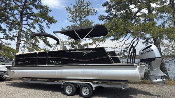 2022 Premier 250 Solaris pontoon boat with Honda outboard motor on trailer, parked by trees.