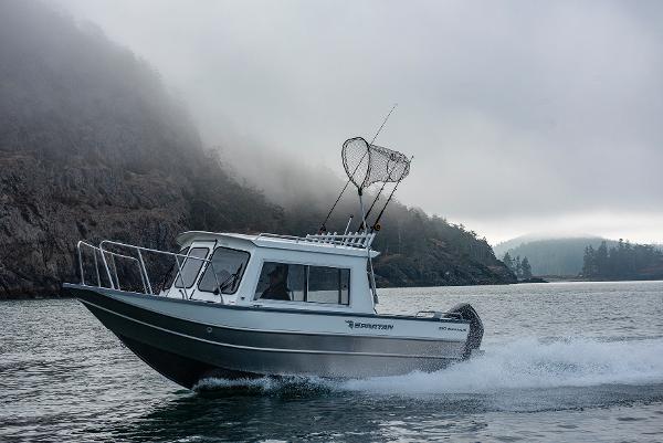 2023 Spartan 220 Maximus Pro boat cruising on misty water near rocky shore.