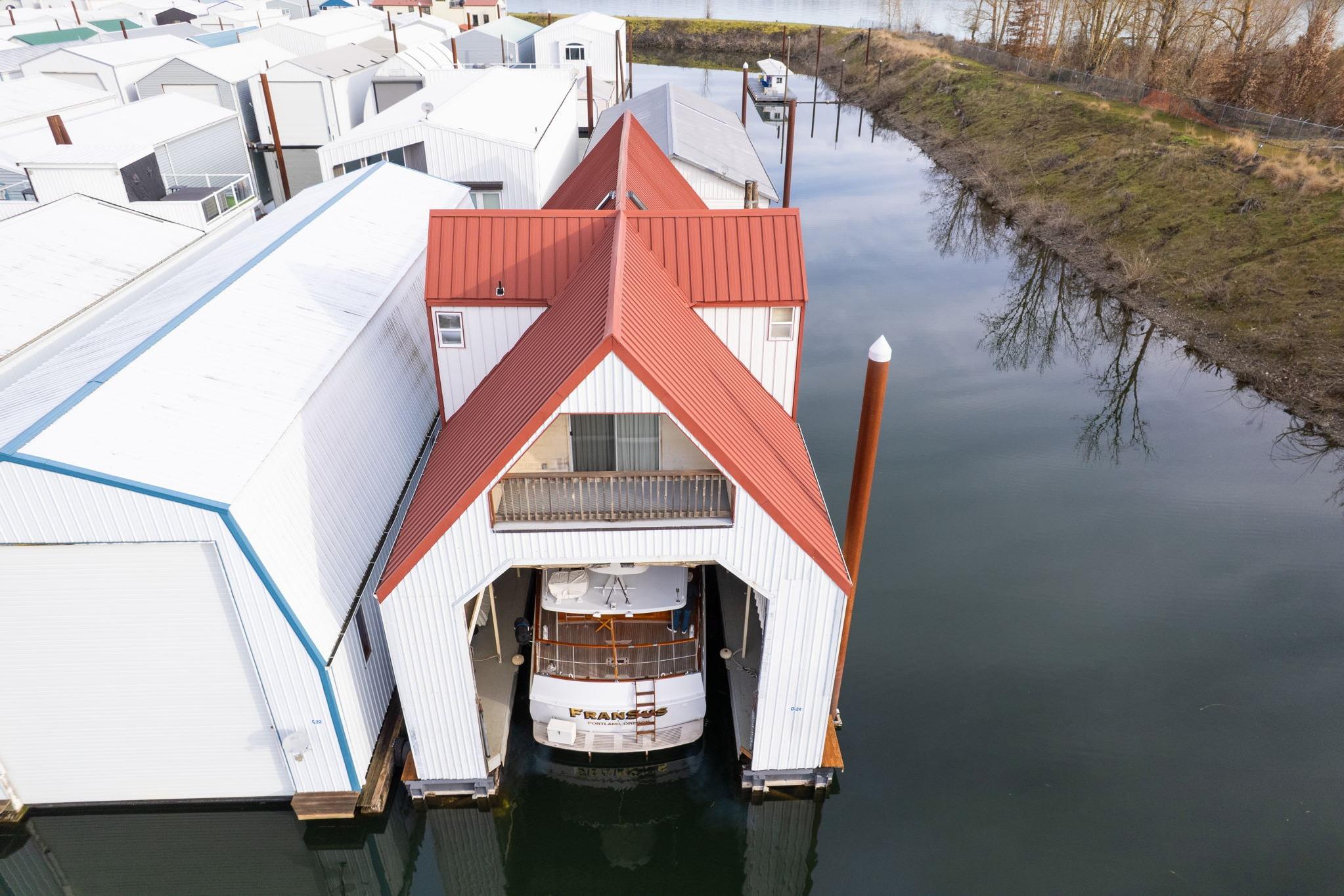 Aerial view of a 1976 custom boathouse with red roof, housing a boat on calm water.