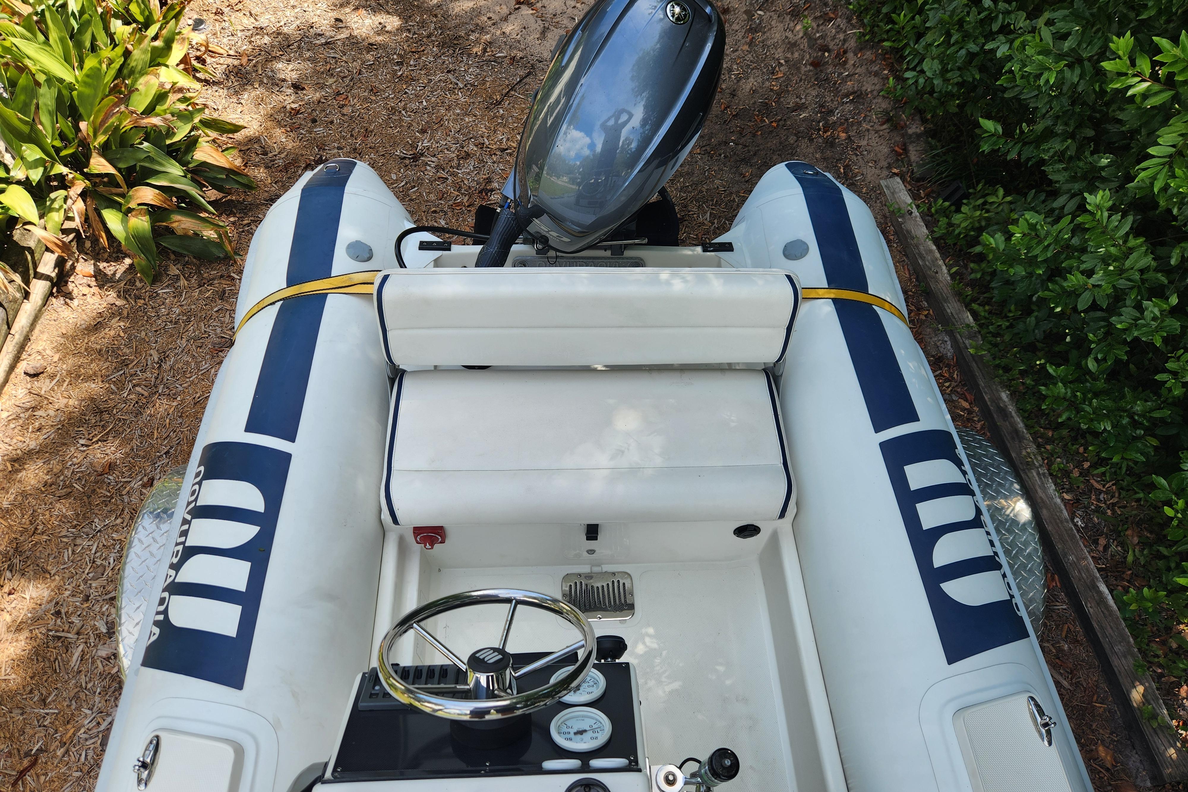 2019 Novurania DL 400 inflatable boat with outboard motor, parked on a leafy shore.