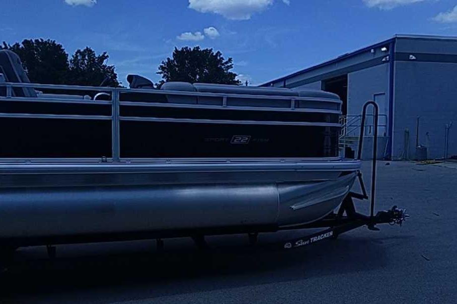 2026 Sun Tracker SportFish 22 DLX pontoon boat parked outside a building under a blue sky.
