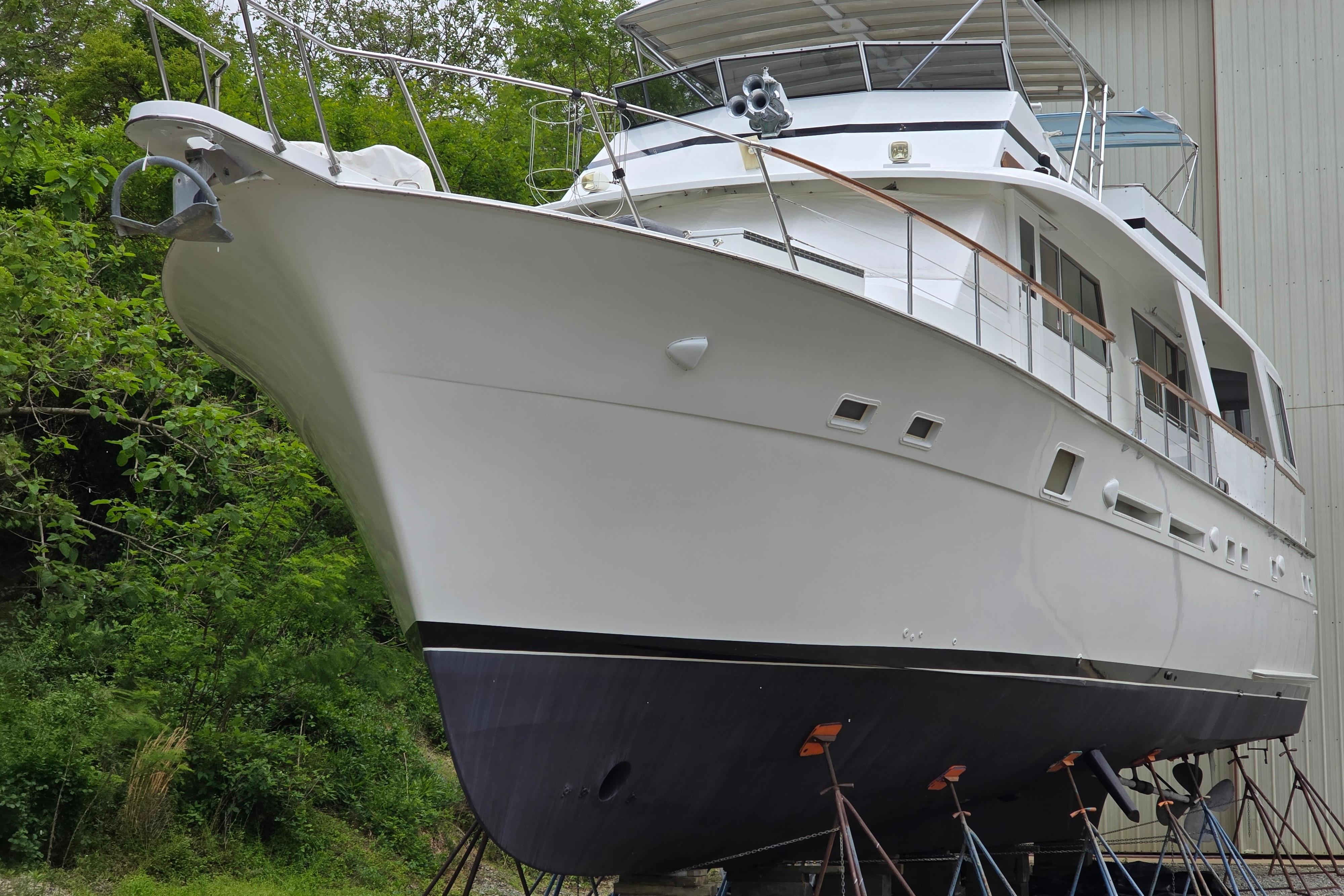 1980 Hatteras 70 Motor Yacht on stands, surrounded by greenery and a building.