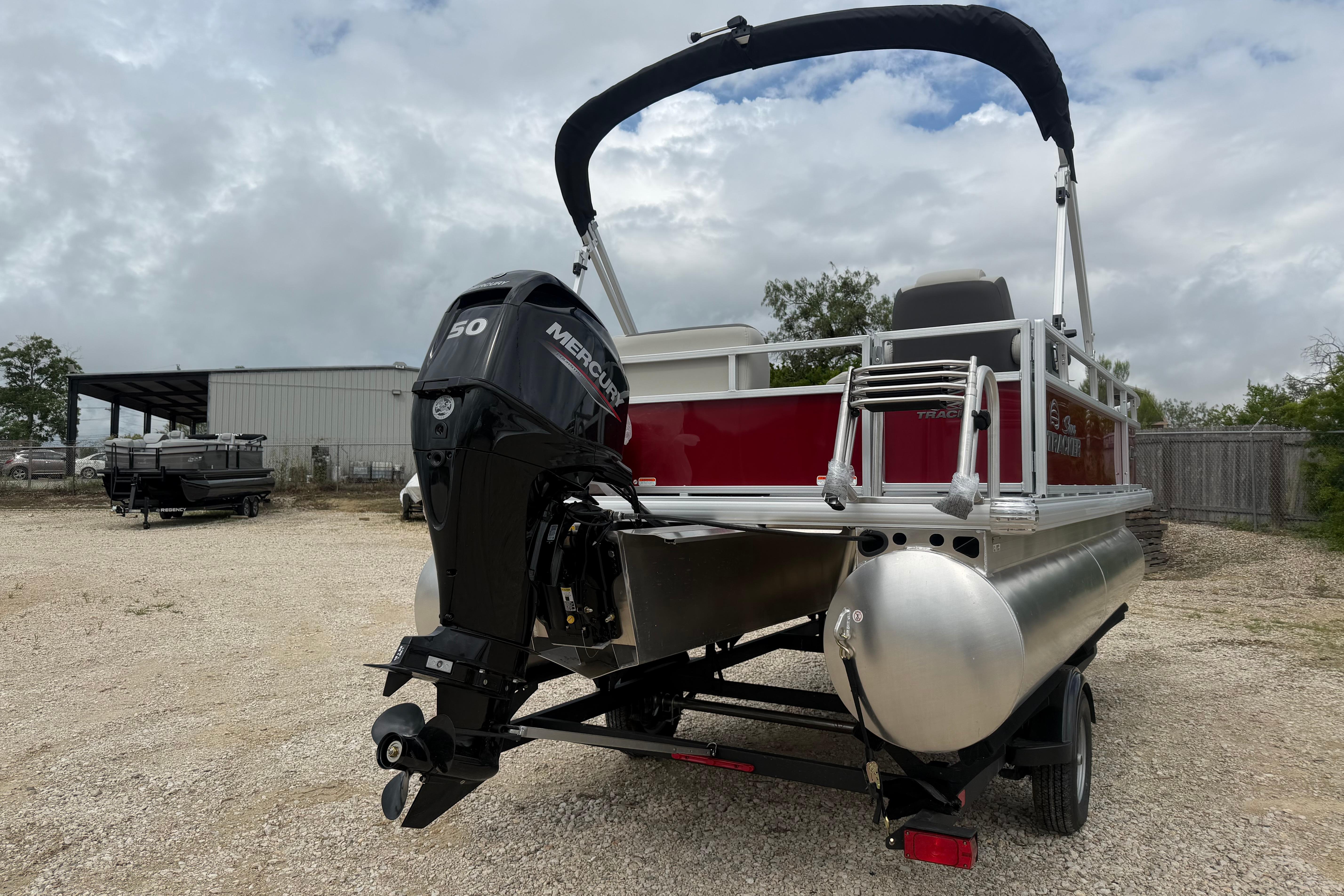 2026 Sun Tracker Bass Buggy 16 XL Select pontoon boat with Mercury engine, parked outdoors.