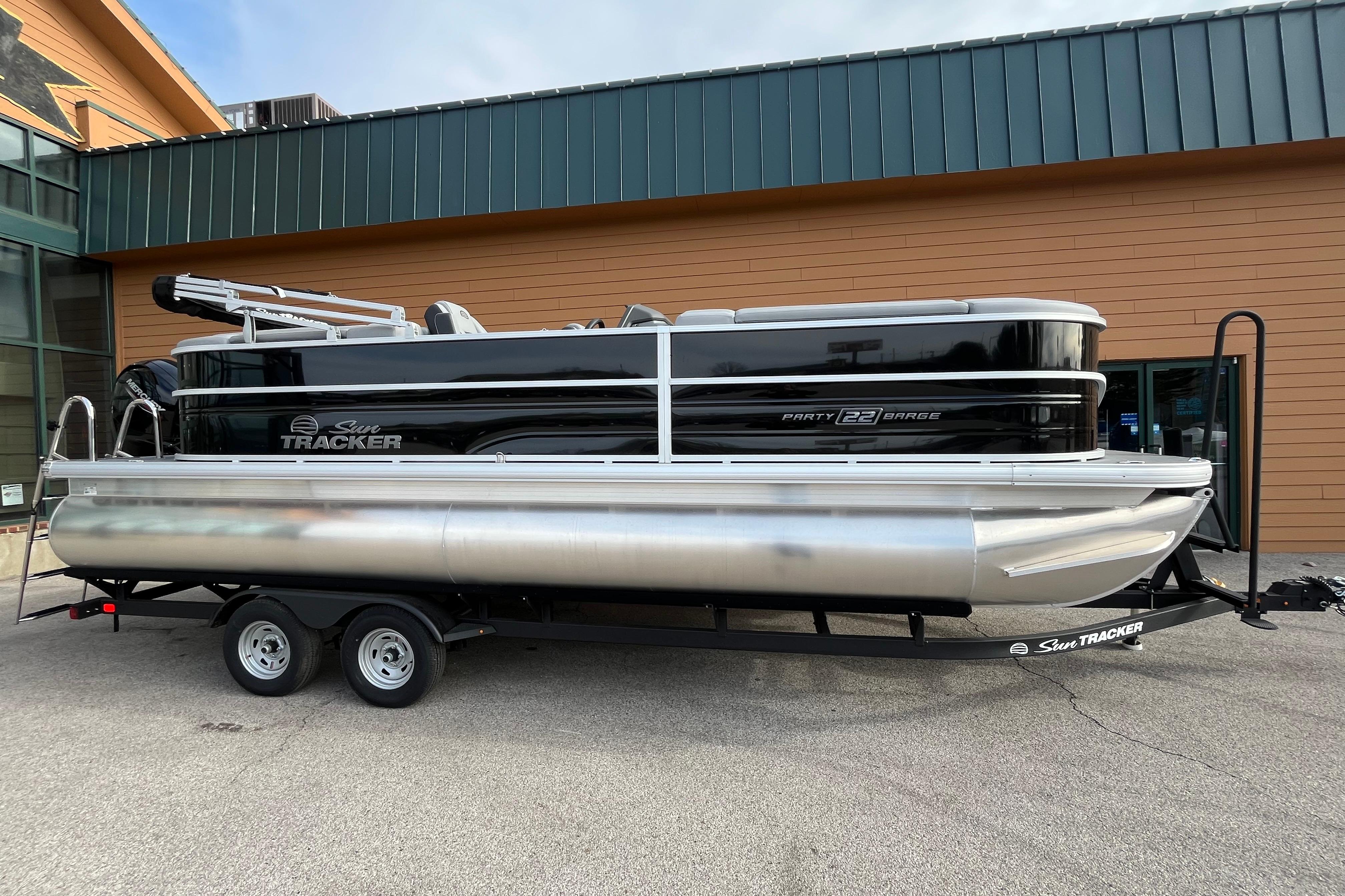2026 Sun Tracker Party Barge 22 DLX pontoon boat on trailer, parked outside building.