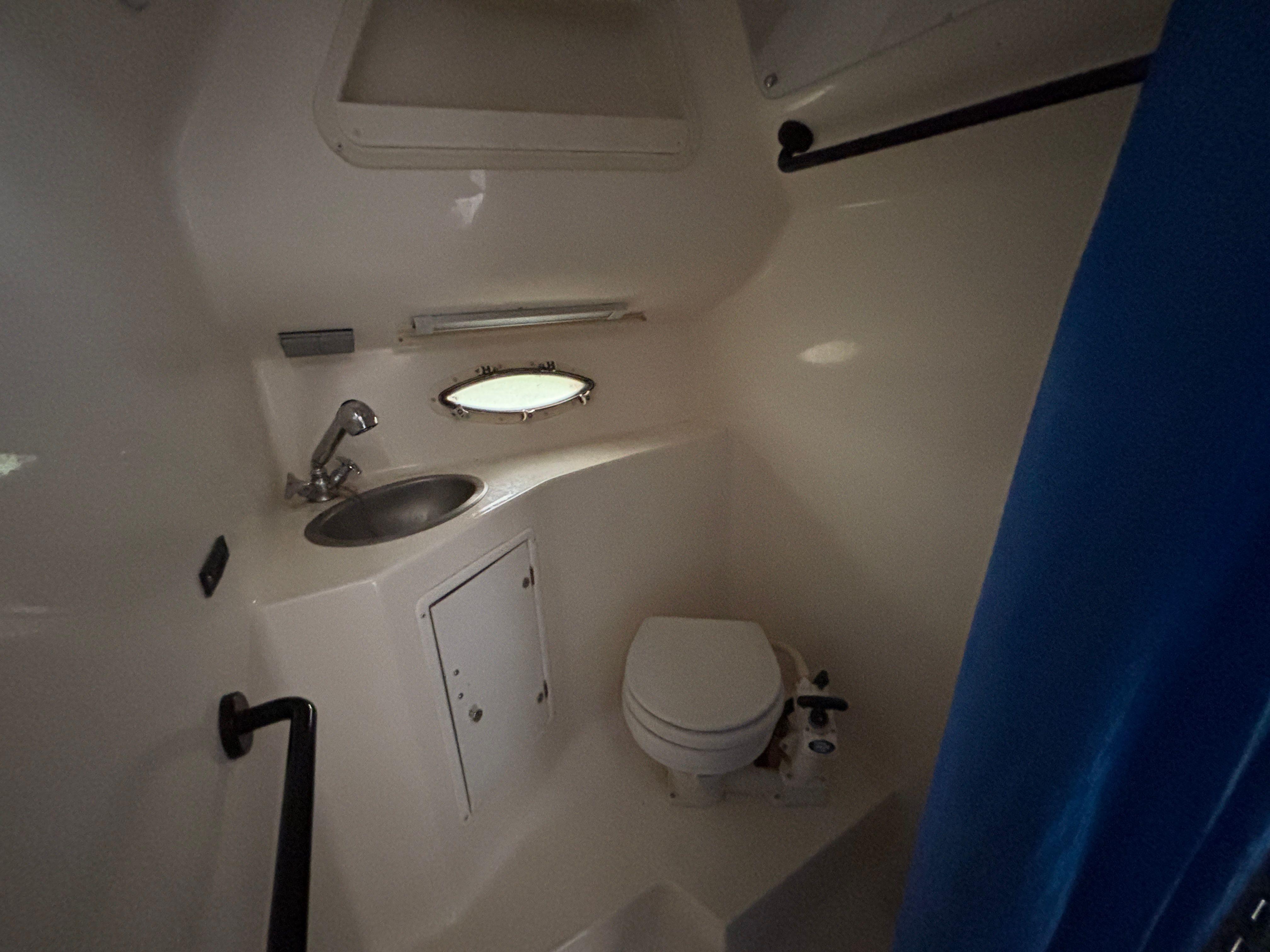 Interior of a boat cabin with a sink, toilet, and porthole.