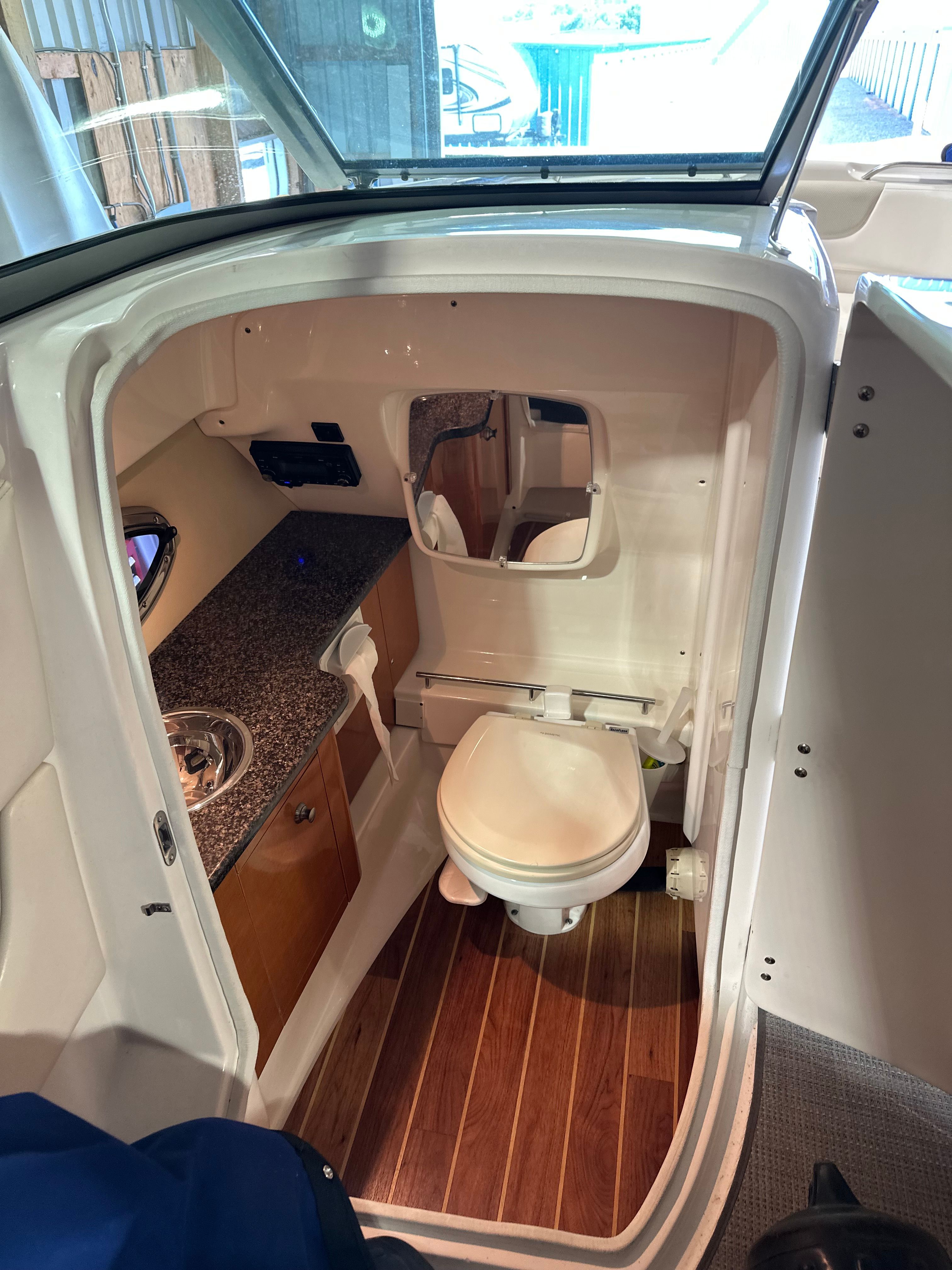 Interior view of a boat bathroom with toilet, sink, and wood flooring.