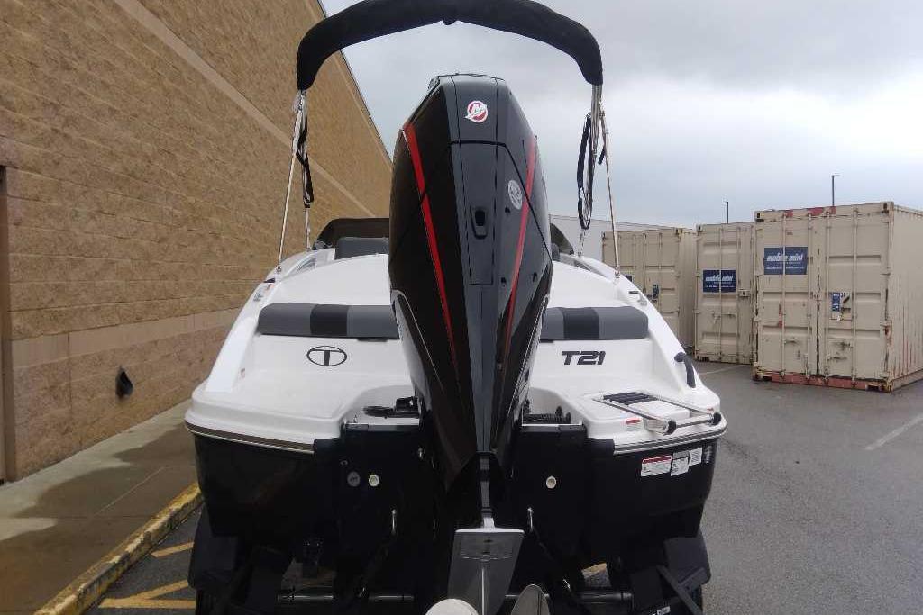 2026 Tahoe T21 boat with outboard motor, parked near storage containers.
