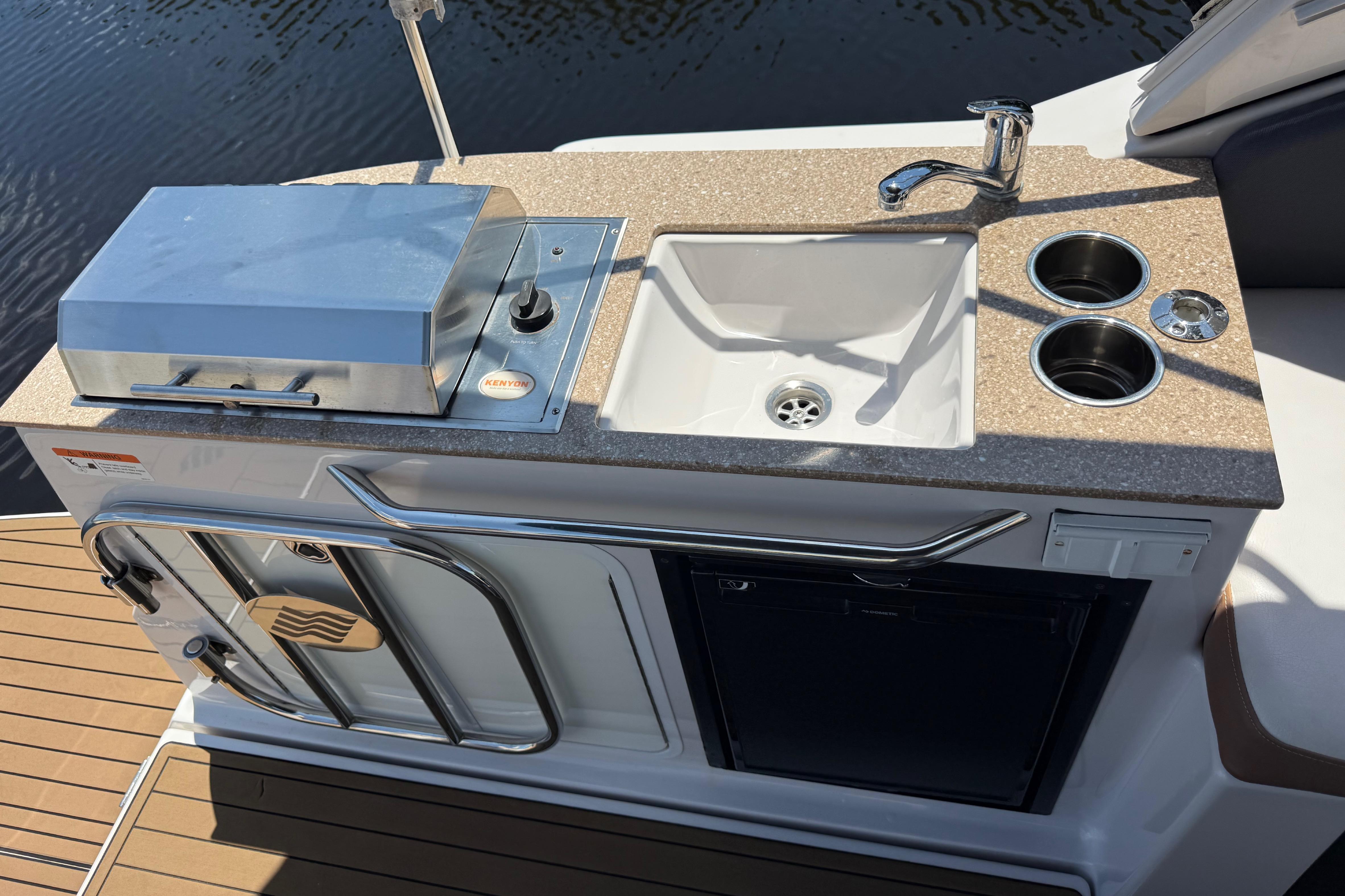 Outdoor kitchenette on 2017 Four Winns V275 boat with grill, sink, and cup holders.