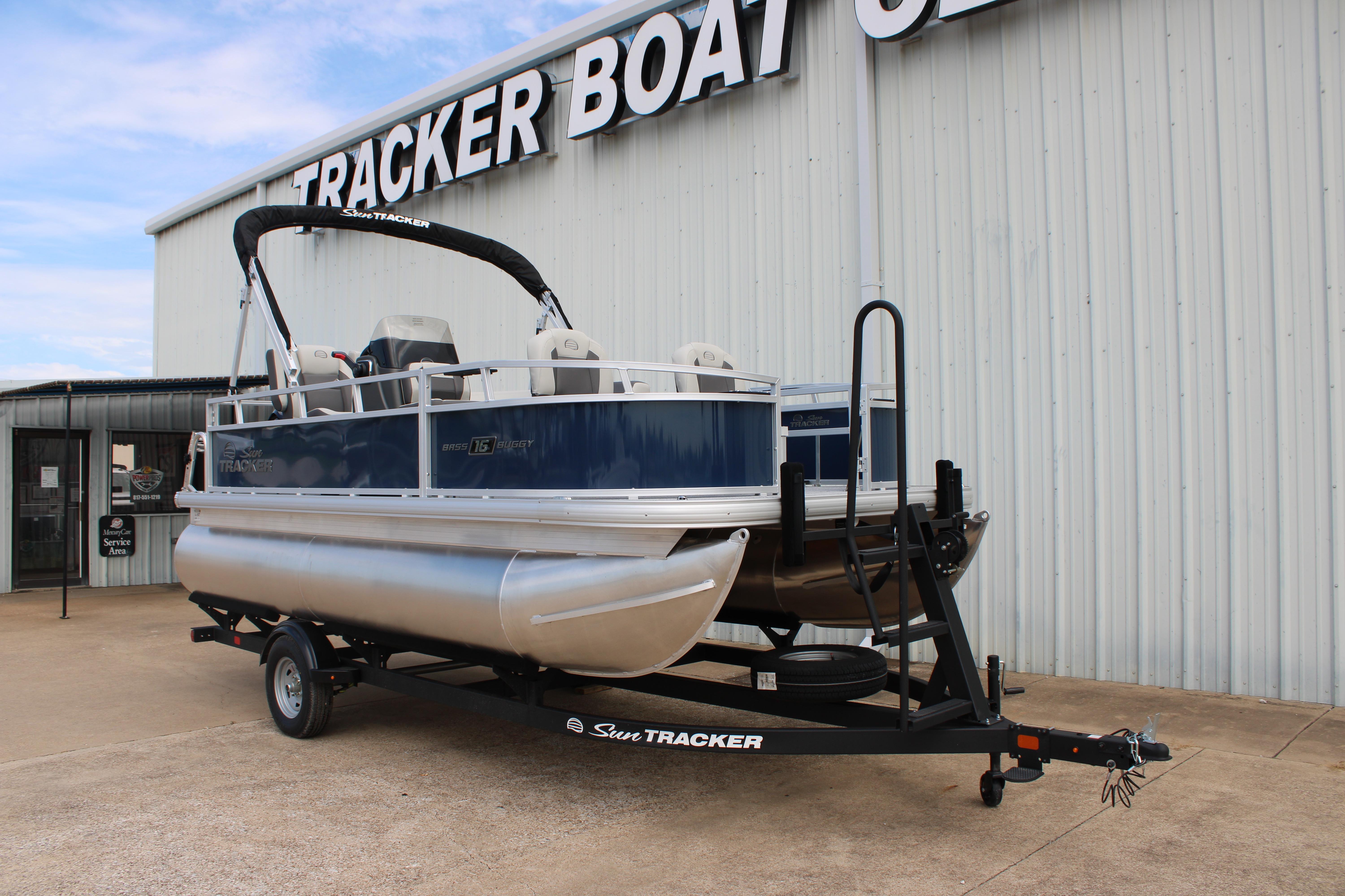 2026 Sun Tracker Bass Buggy 16 XL Select pontoon boat on trailer outside dealership.