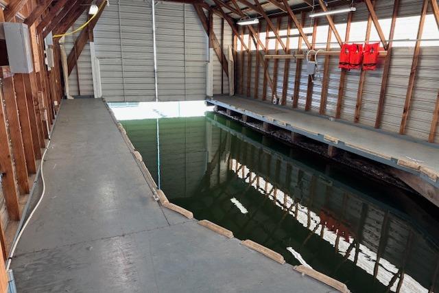 1960 custom boathouse interior with dock, water channel, and life jackets on wooden walls.
