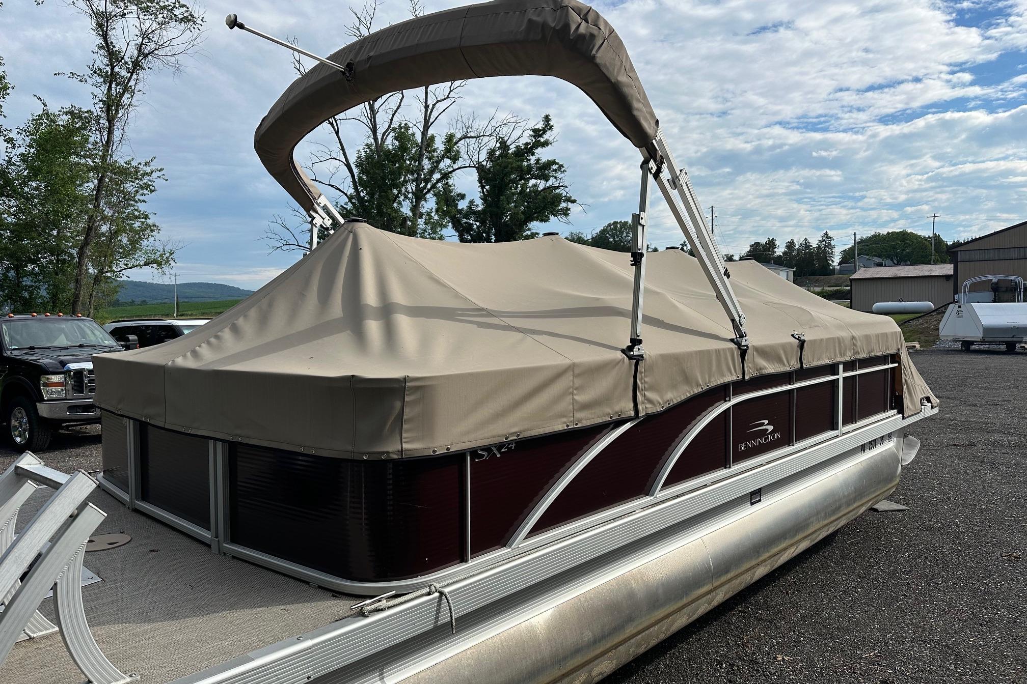 2016 Bennington 24 SCWX pontoon boat with beige cover, parked outdoors.
