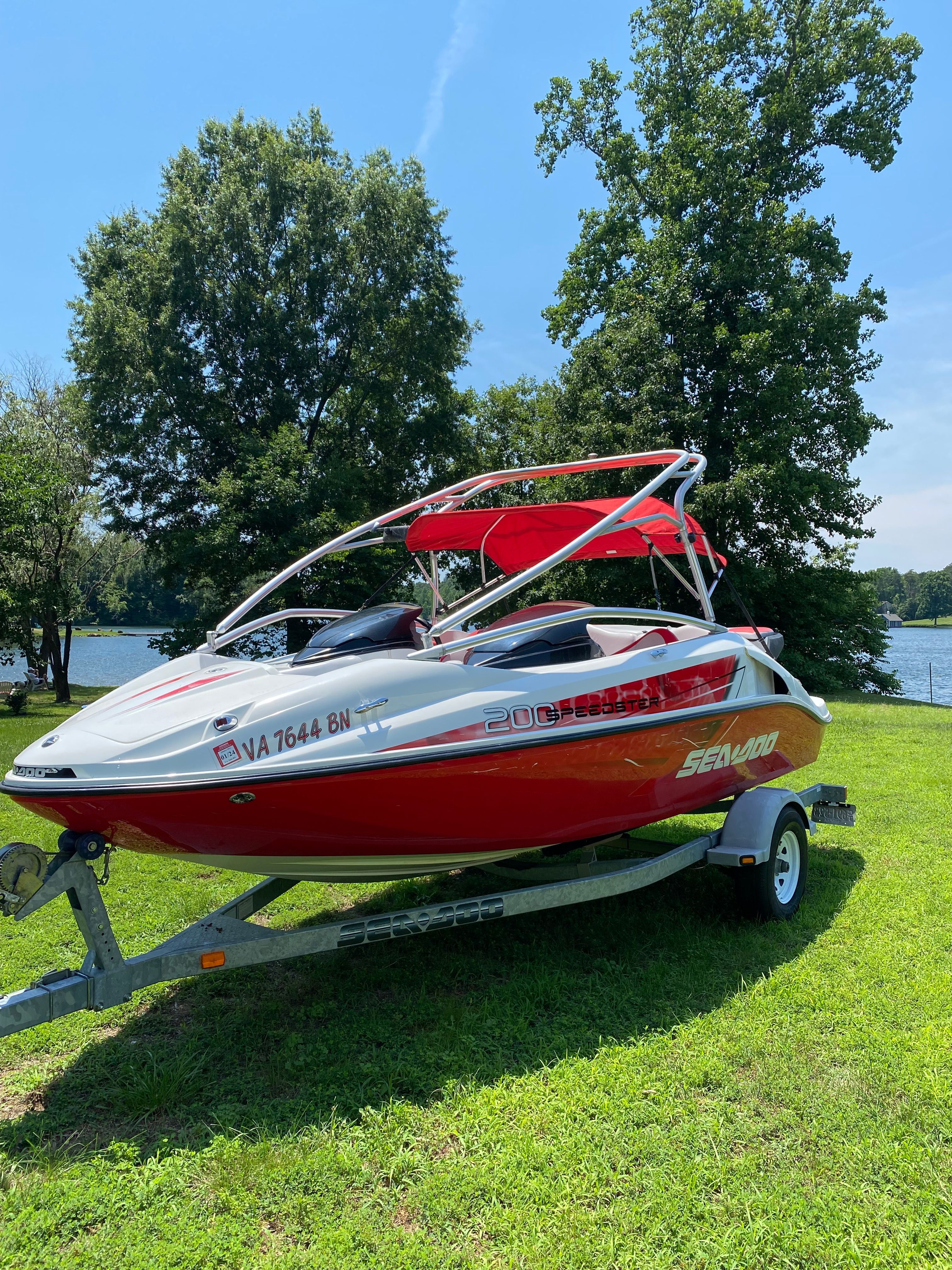 A red 2008 Sea-Doo Speedster 200 boat on a trailer on a grassy area.
