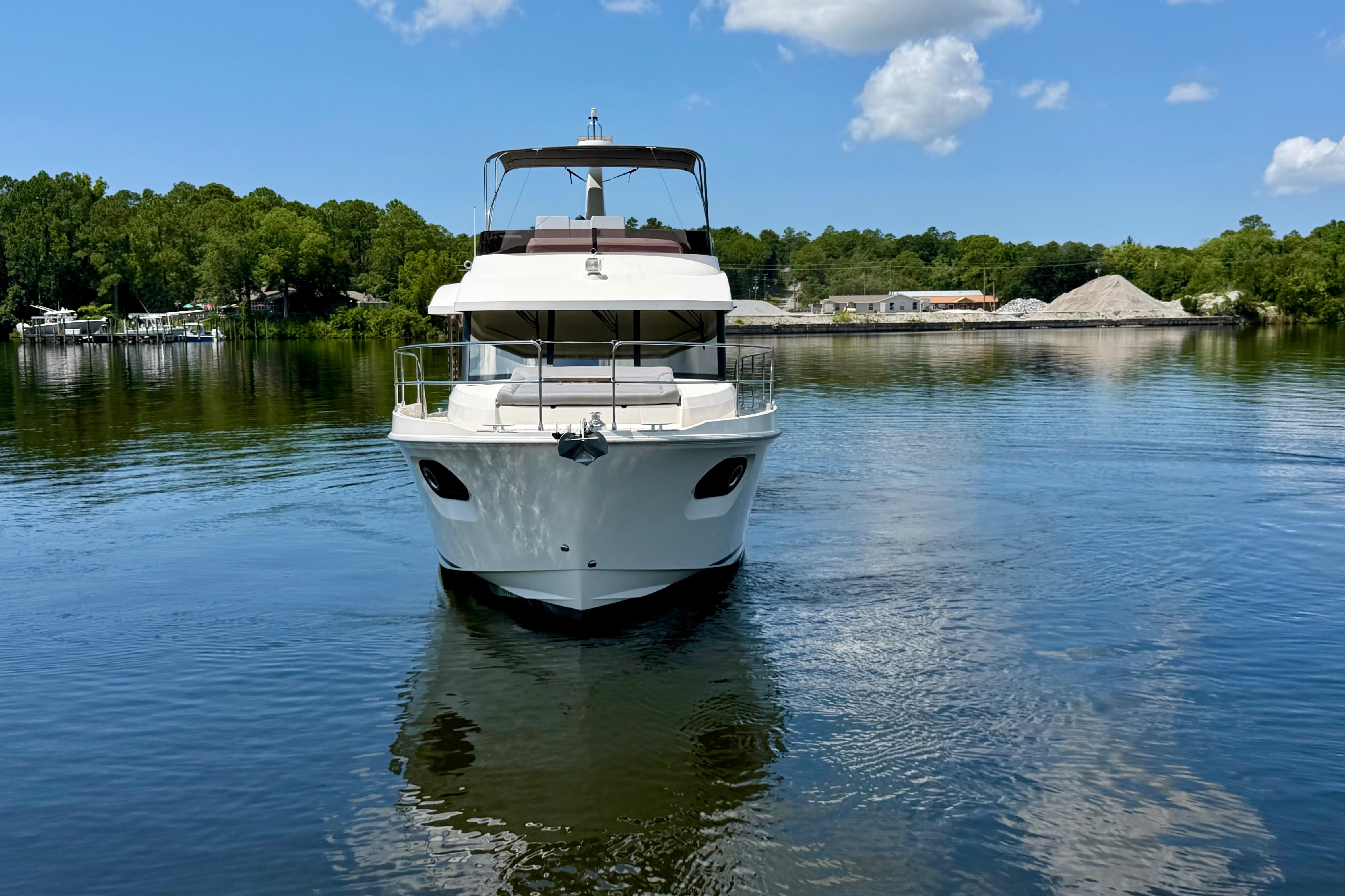 2025 Beneteau Swift Trawler 41 Fly on serene water, surrounded by lush greenery.