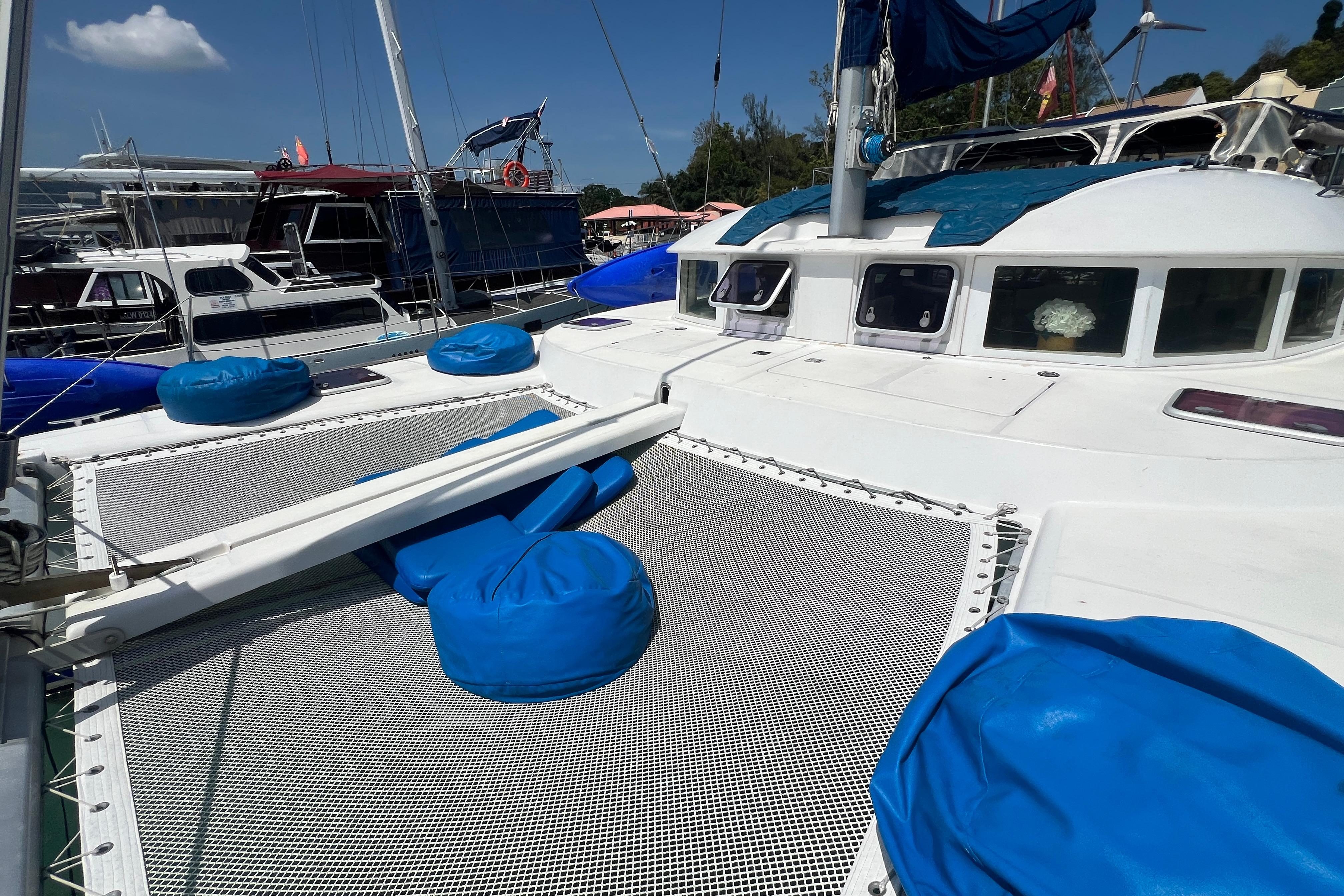 2003 Lagoon 380 catamaran with blue cushions, docked in a marina under clear skies.