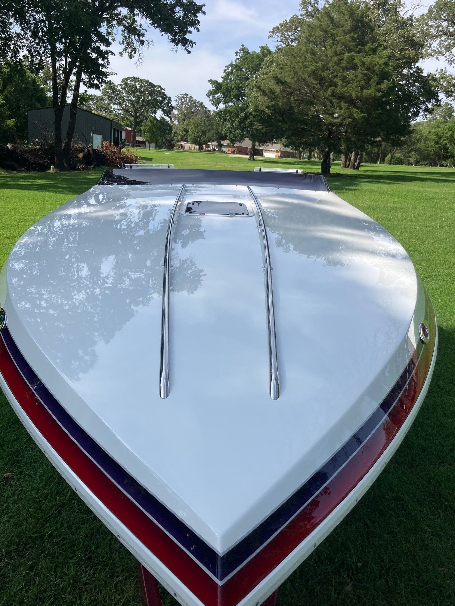 A white boat with red and blue stripes is on a green lawn.