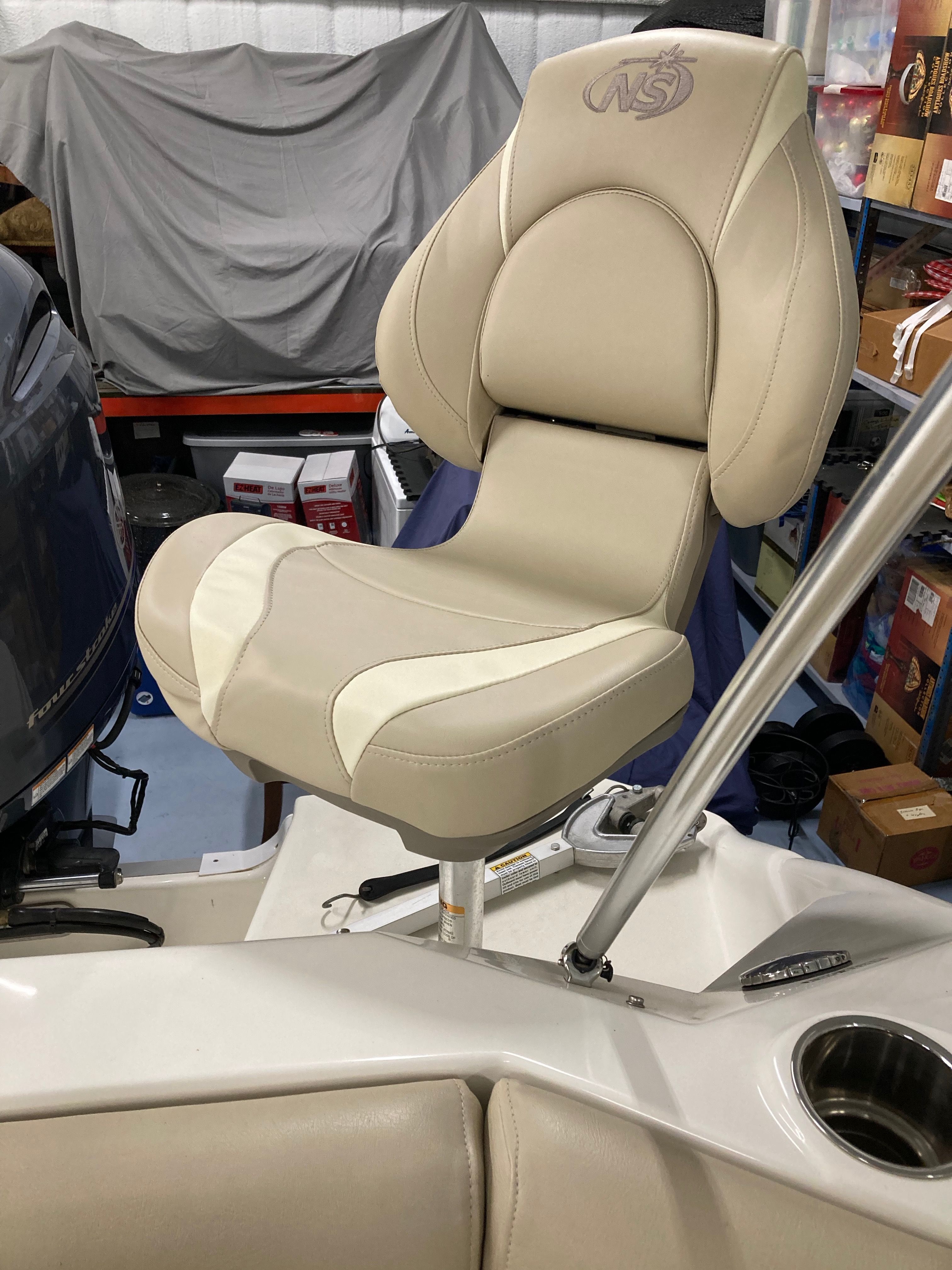 Beige boat seat with high backrest and armrests, surrounded by equipment and accessories.